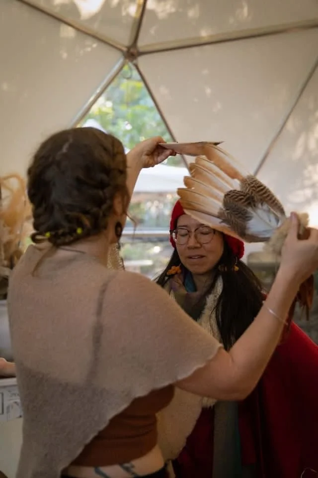 Two women in a tent, one in a feathered headdress, participating in a cultural or spiritual ceremony.
