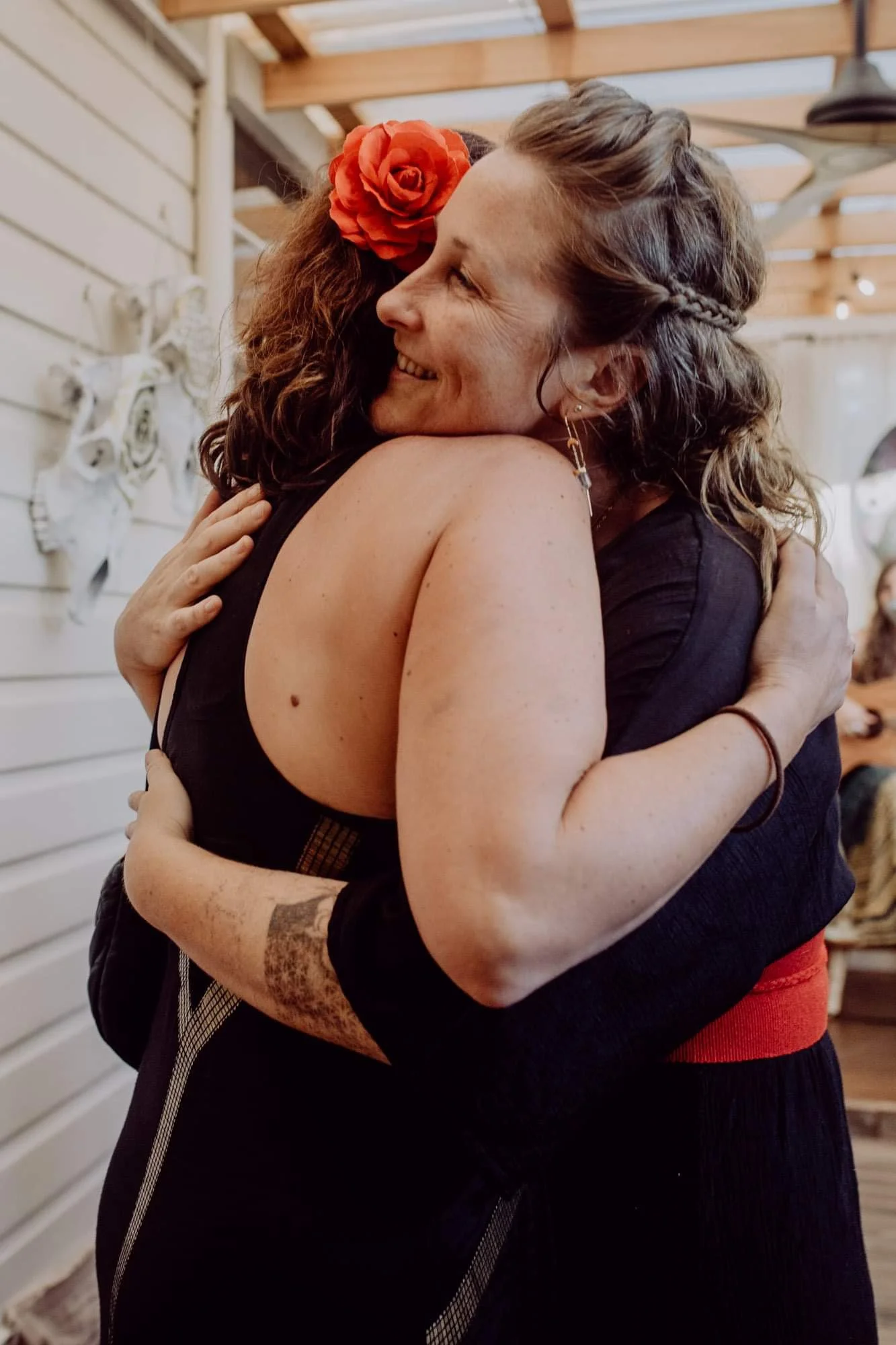 Two women are hugging each other warmly, smiling, and showing affection in a cozy indoor setting.