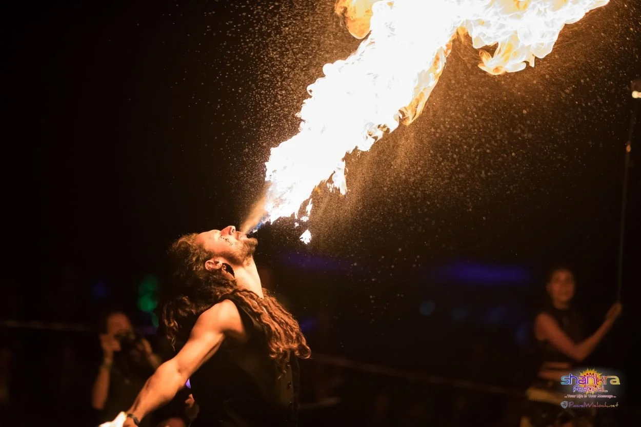 Feuerspeier bei einer Show, der eine Flammenzunge aus seinem Mund spuckt, bei Nacht