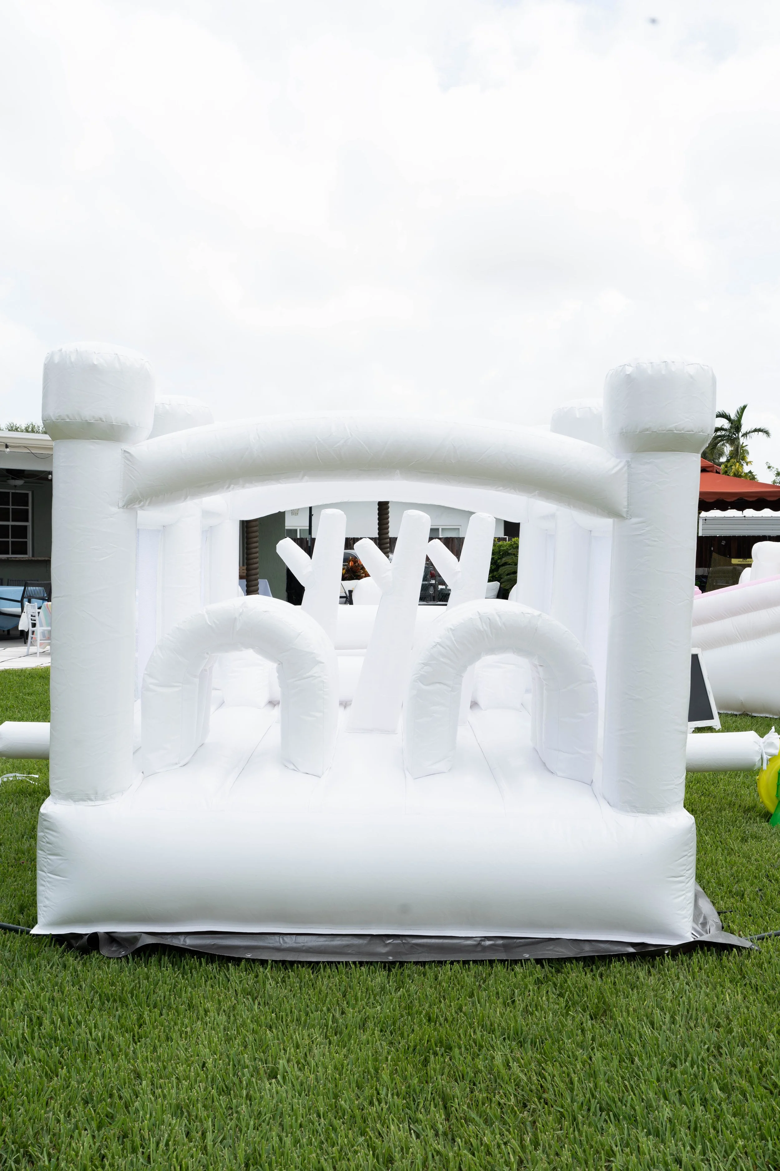 White inflatable bounce house designed to resemble a castle with towers and arched entryway, set up on a grassy area outdoors.