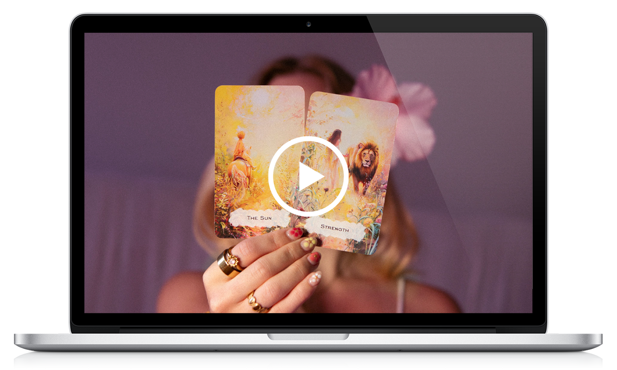 A woman holding two tarot cards, titled "The Sun" and "Strength," in front of her face on a laptop screen