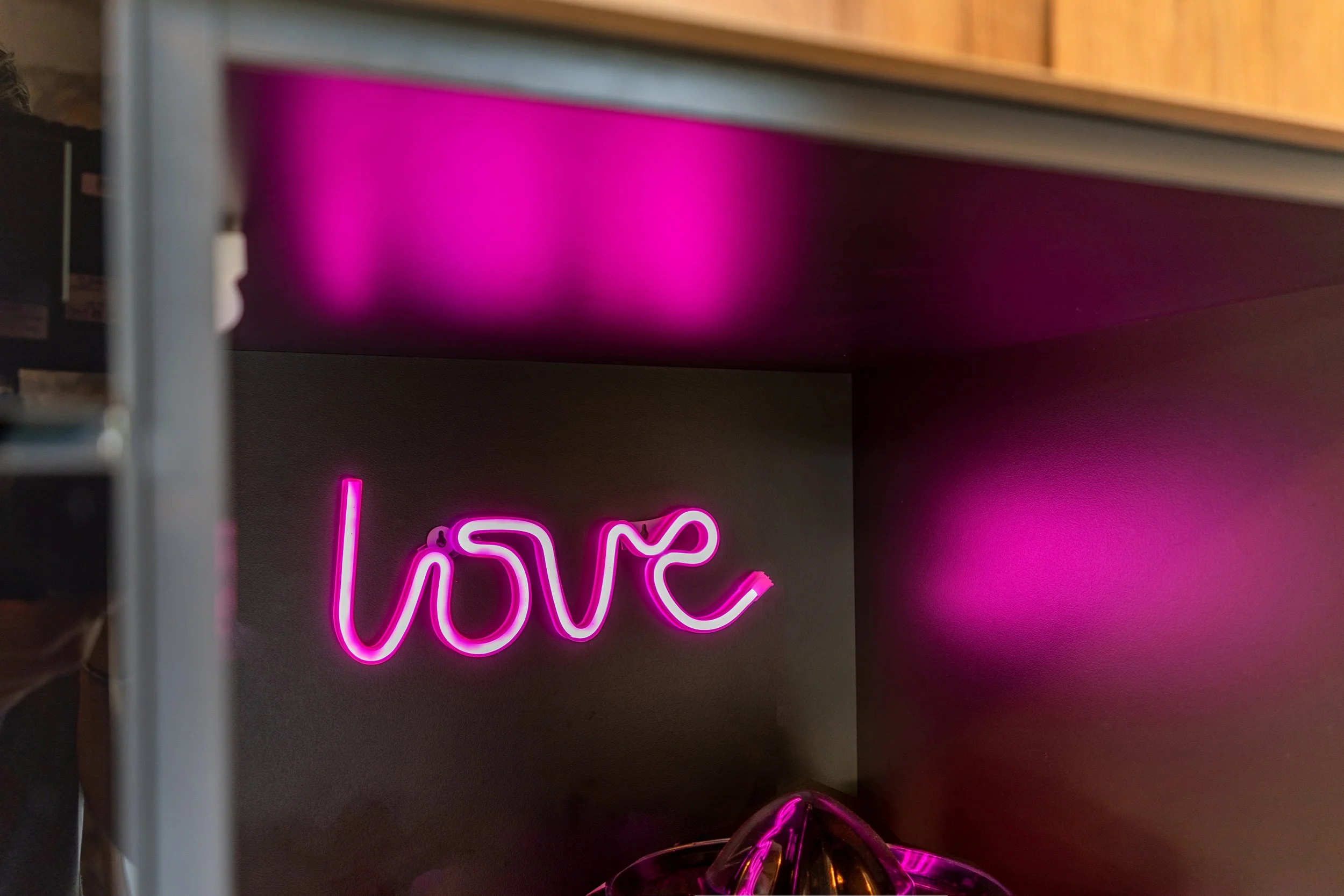 Neon pink sign spelling 'love' on a dark wall with pink reflections.