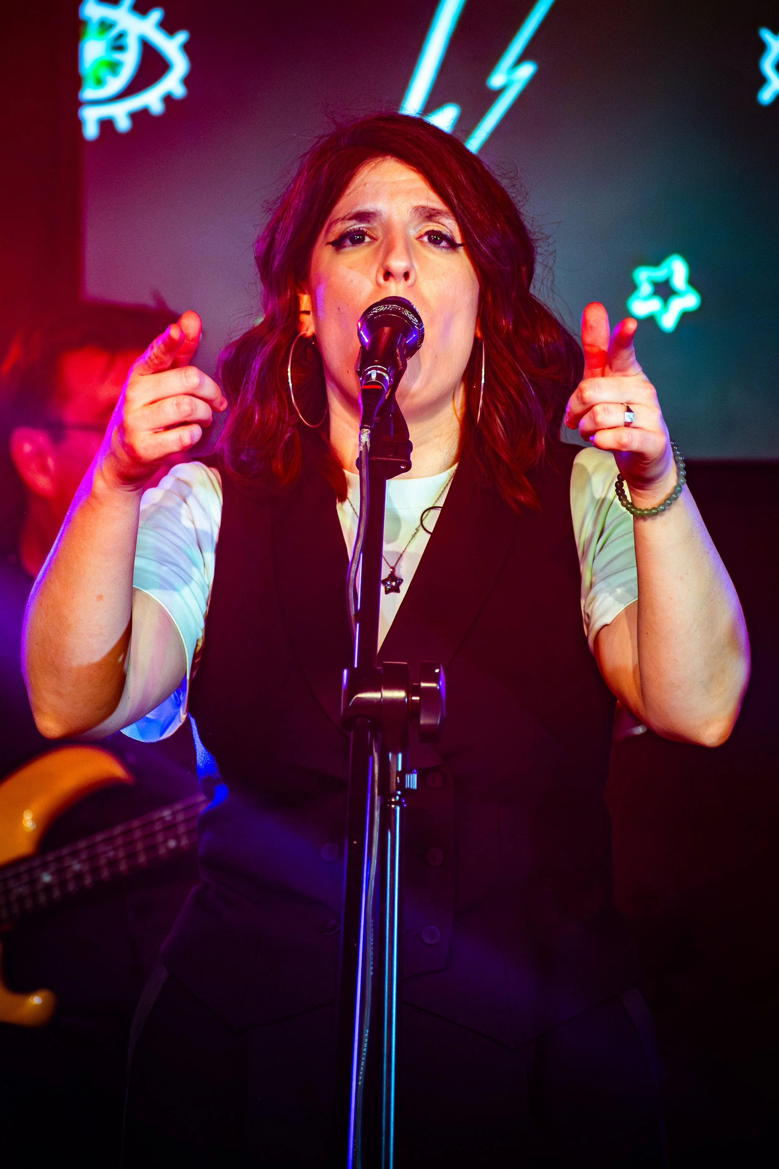 A woman singing into a microphone on stage with neon decorations in the background.