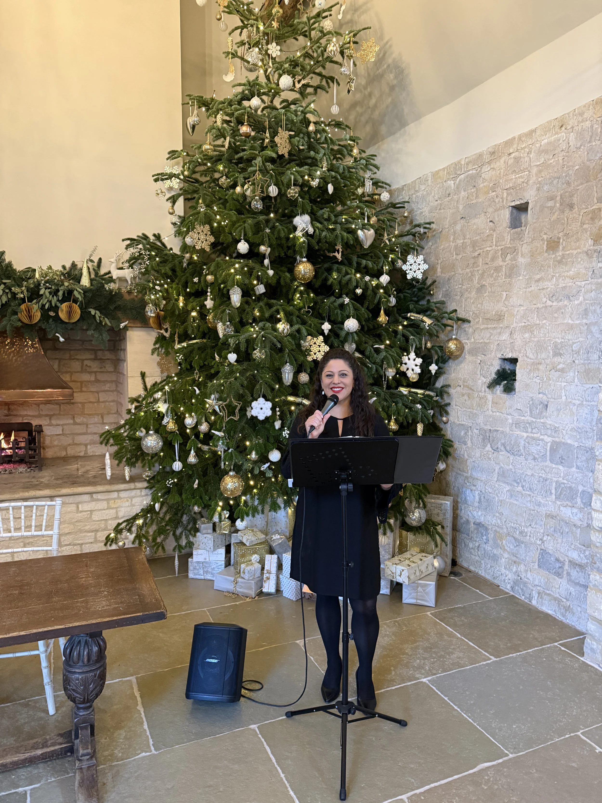 Tricia Rosas singing in front of a tall, beautifully decorated Christmas tree at Blackwell Grange in the Cotswolds, UK.