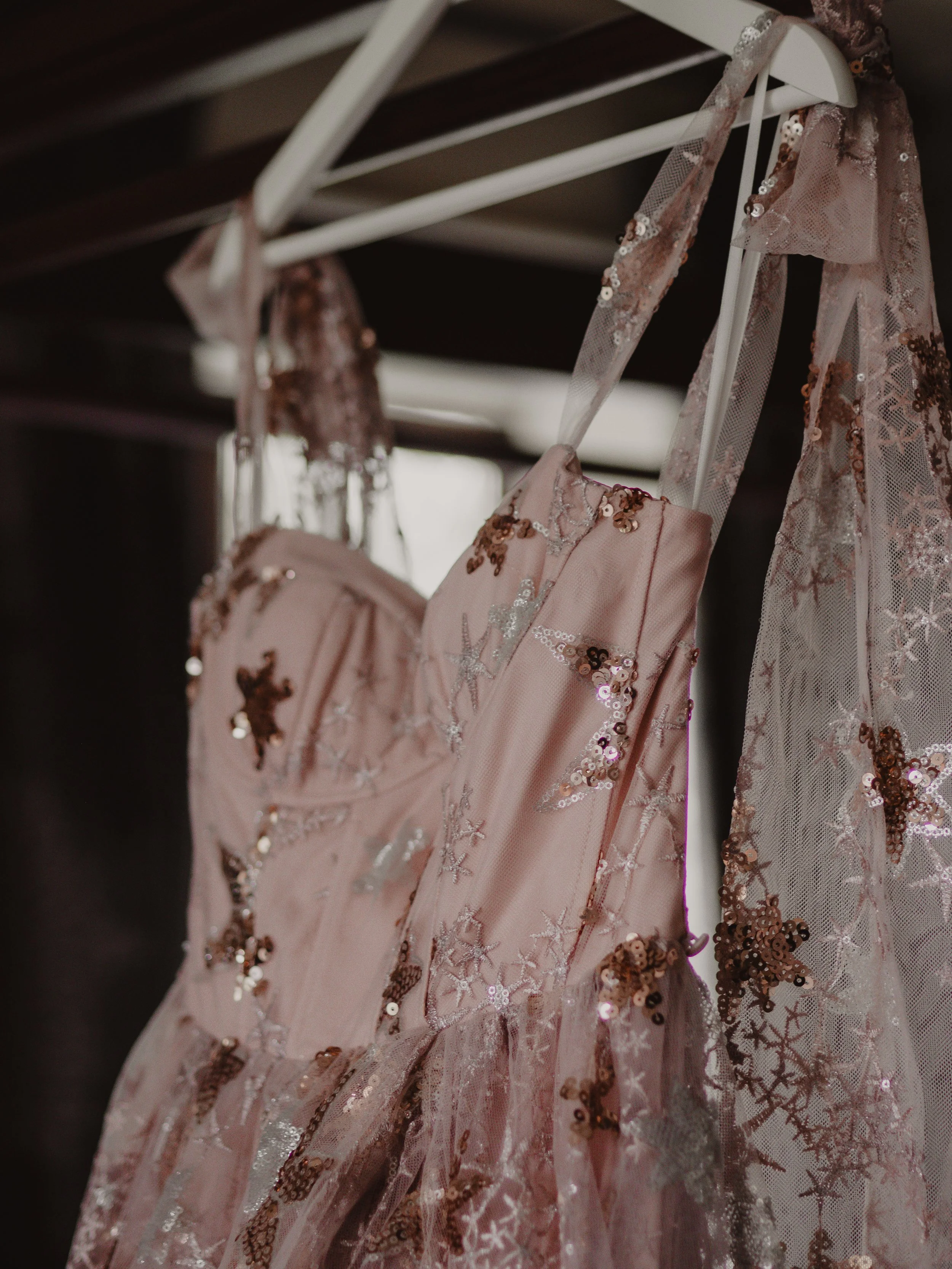A pink strapless dress with sequin and embroidery details hanging on a white hanger.