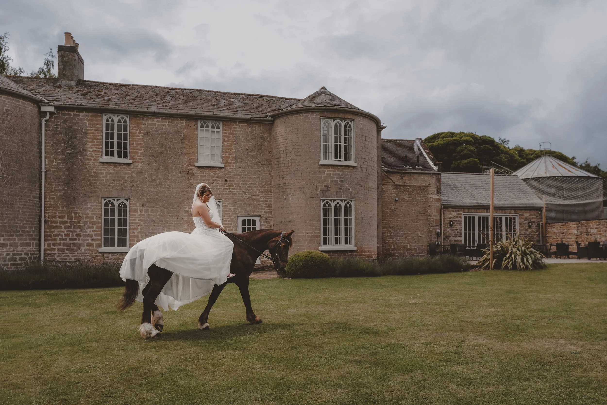 Bride in a white wedding gown riding a horse at Cockliffe Country House.