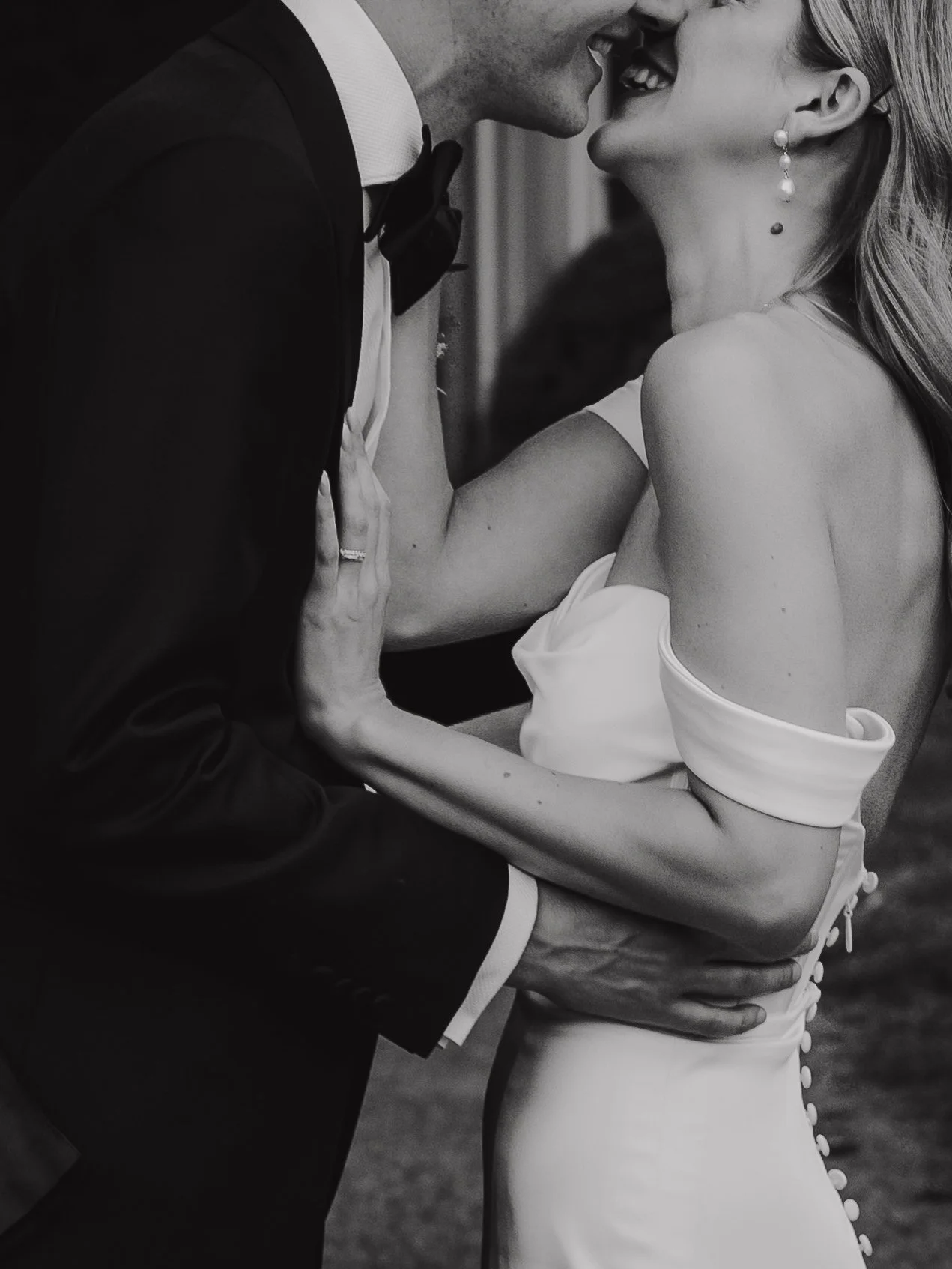 A black and white photo of a bride and groom kissing during their wedding, with the bride holding the groom's face and the groom's hand on her waist.