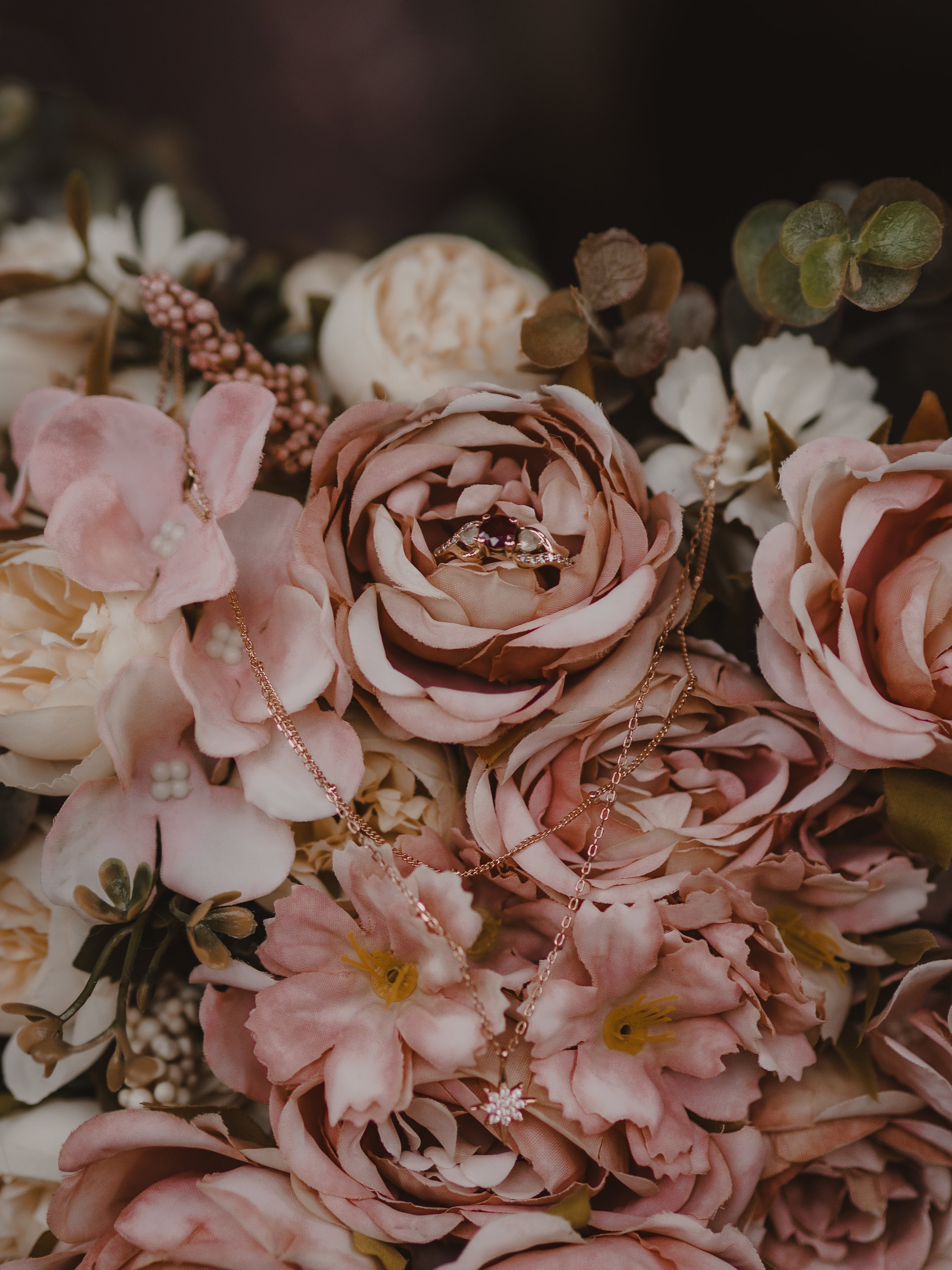 A bouquet of pink and white flowers with jewelry, including a ring and necklaces, displayed among the flowers.