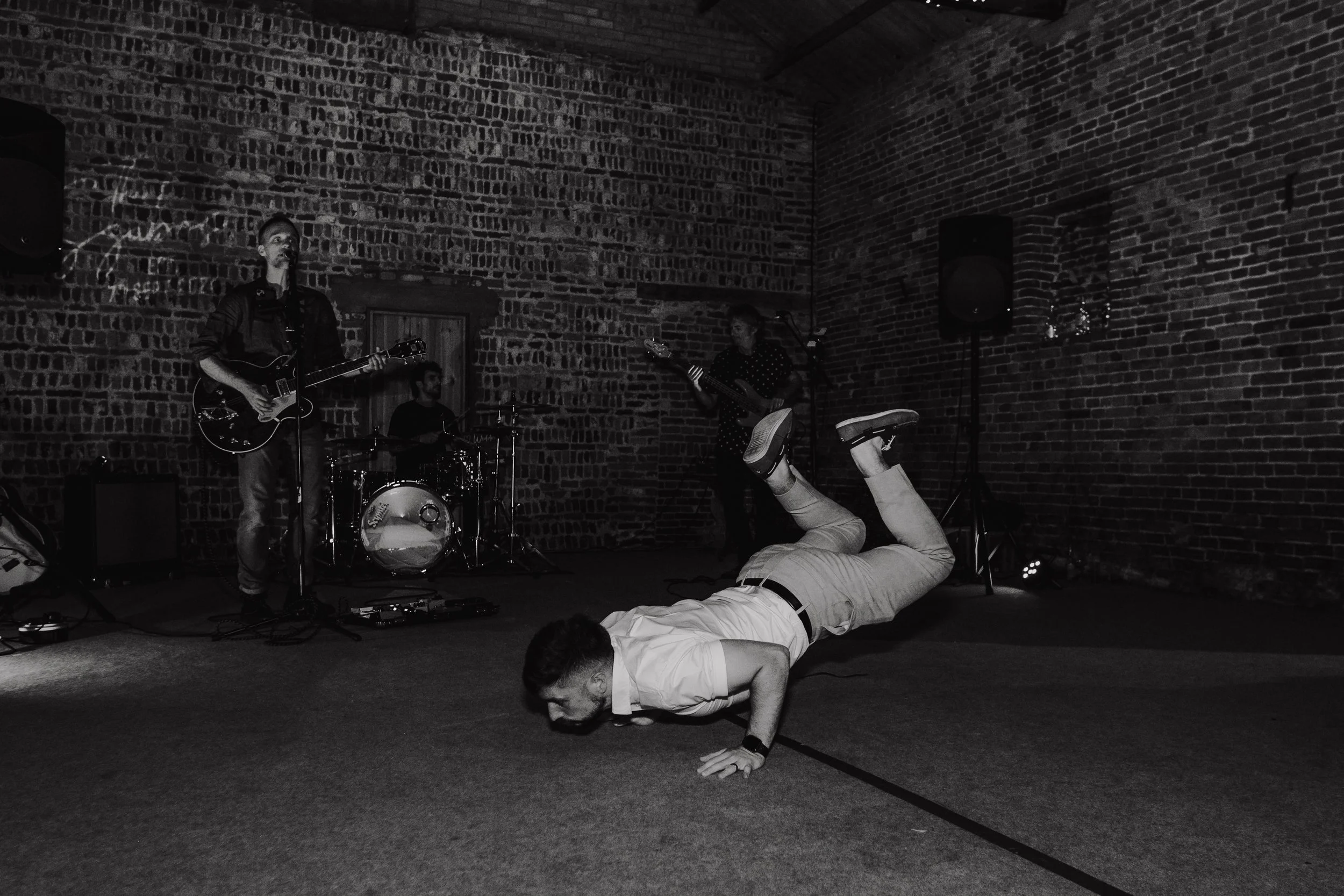 Wedding guest doing the worm on the dance floor in front of a live band playing music in a brick-walled venue.