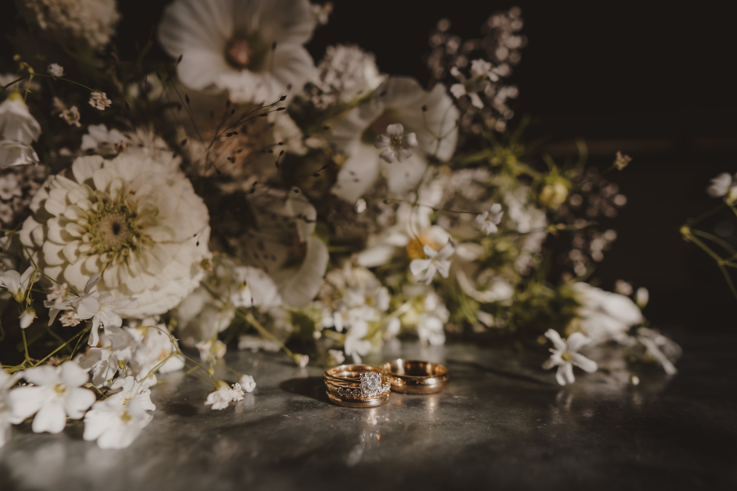 Close-up of wedding rings on a metallic surface with white flowers in the background.