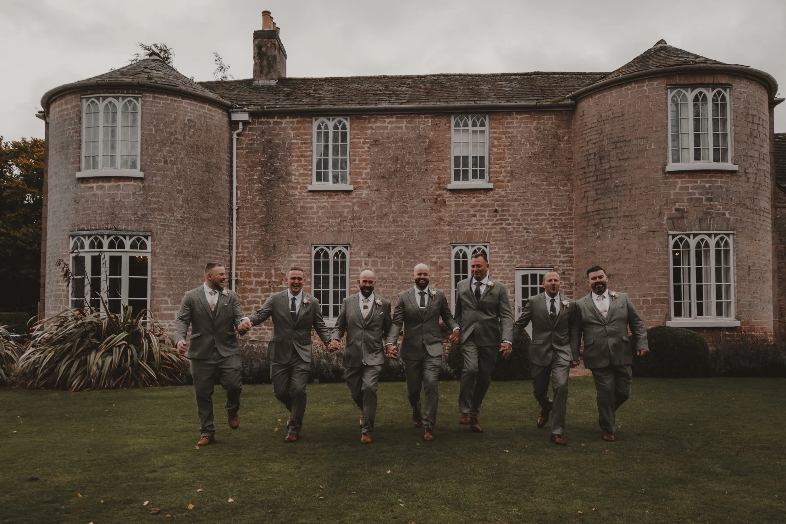 Groom and six groomsmen in matching gray suits skipping at Cockliffe Country House