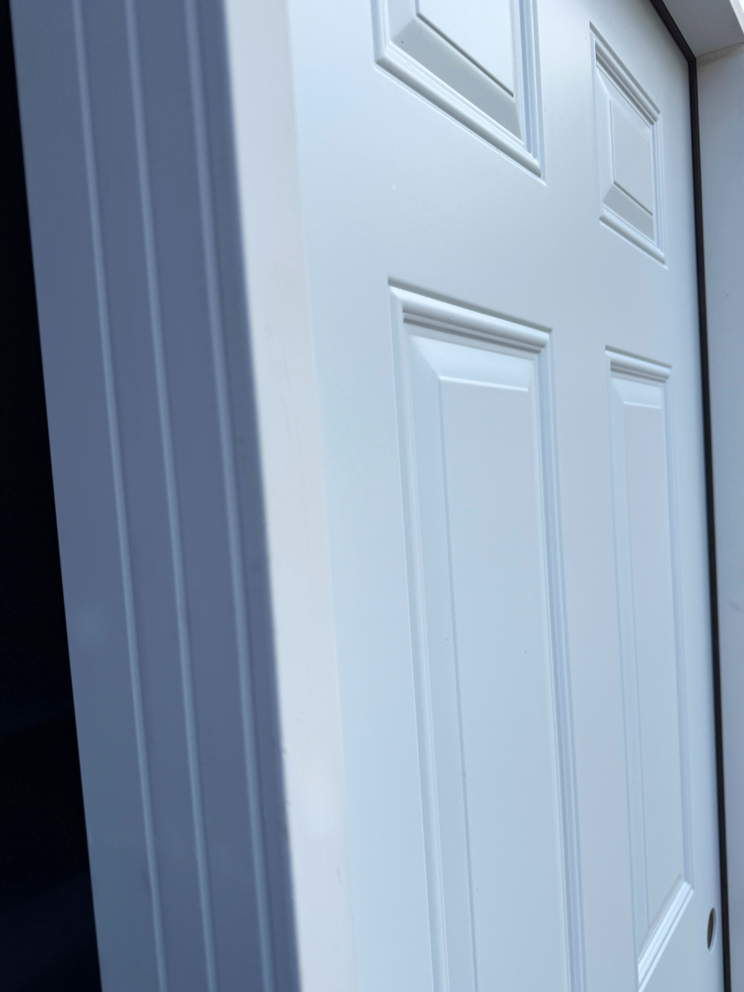 Close-up of a white panel door with decorative molding, set in a white frame, viewed from an angle.