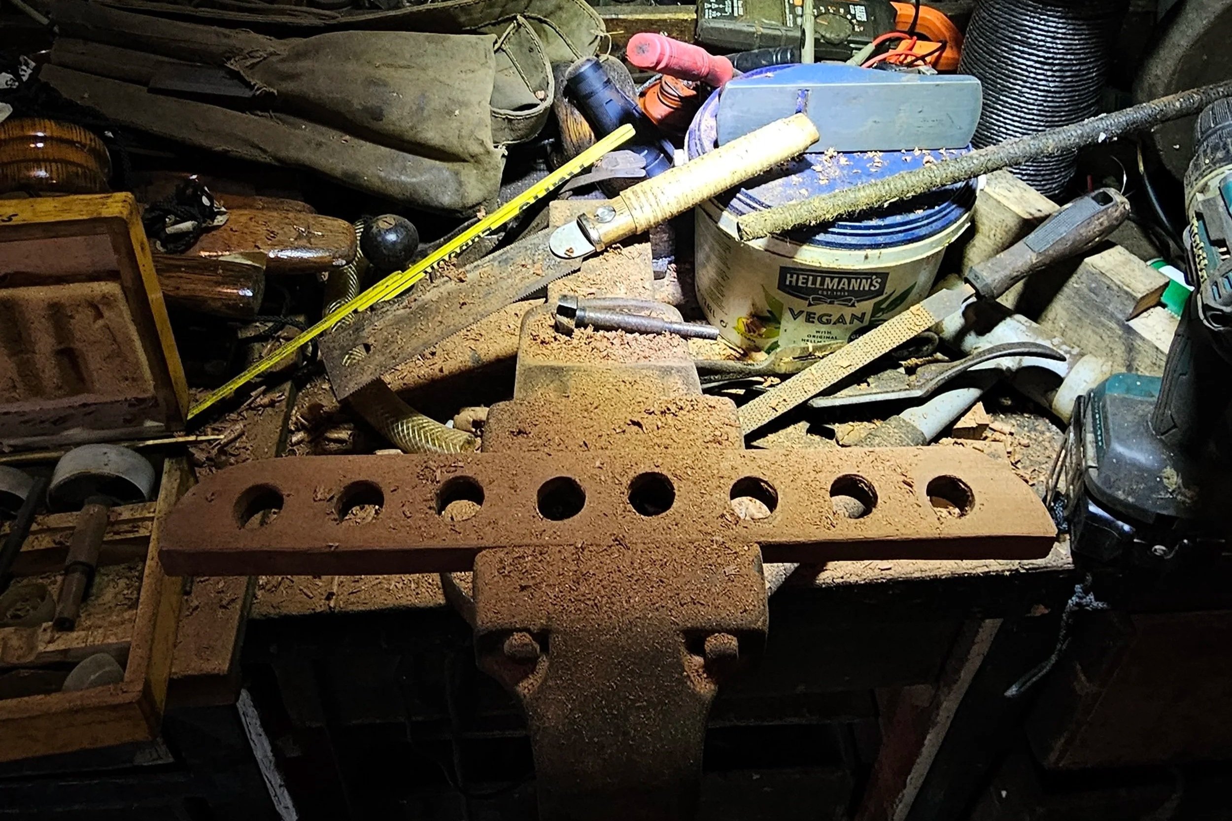 Cluttered workbench with hand tools, containers, and spray cans in a wood workshop.