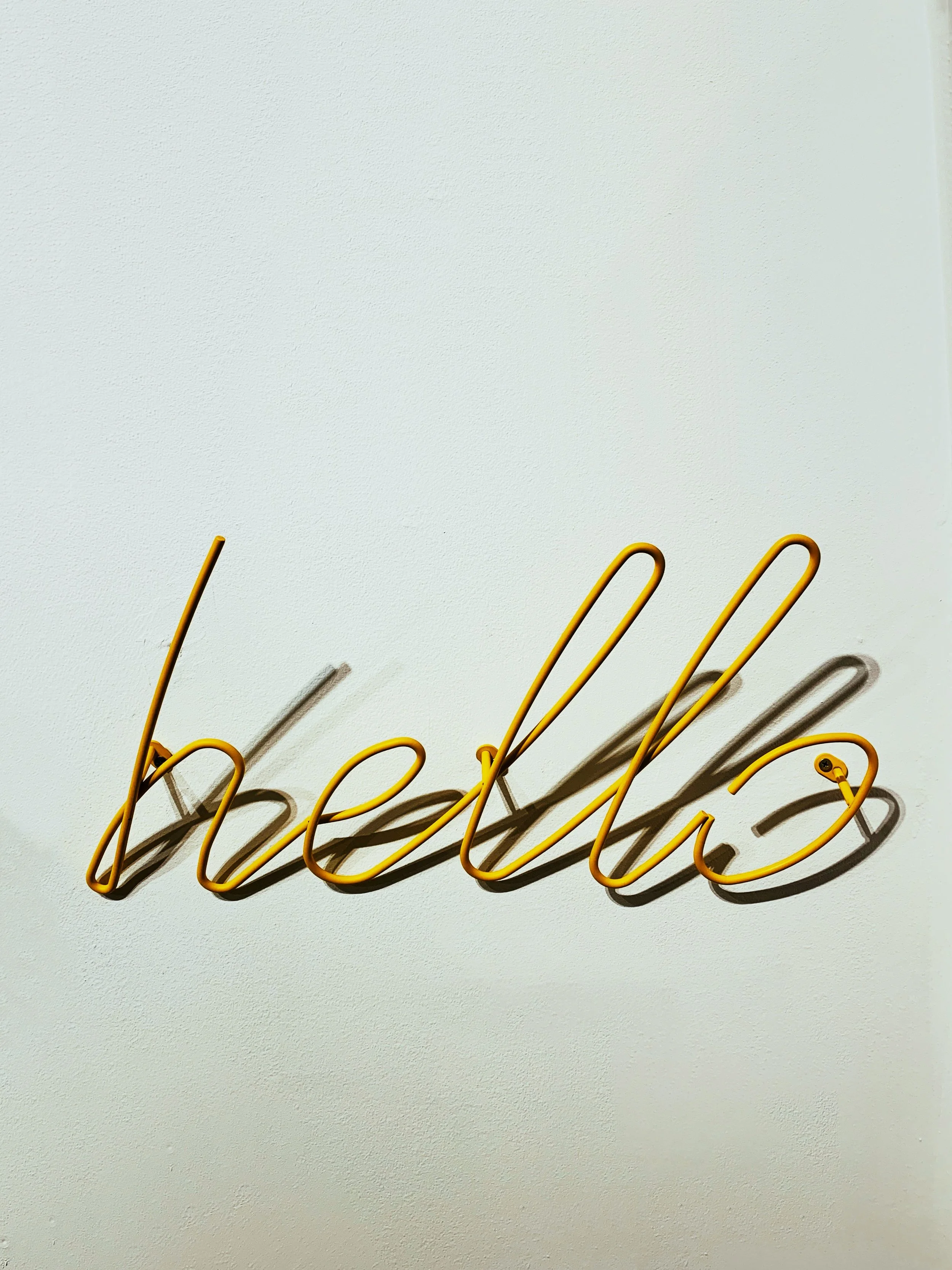 Yellow neon sign spelling 'hello' on a white wall, casting a shadow.