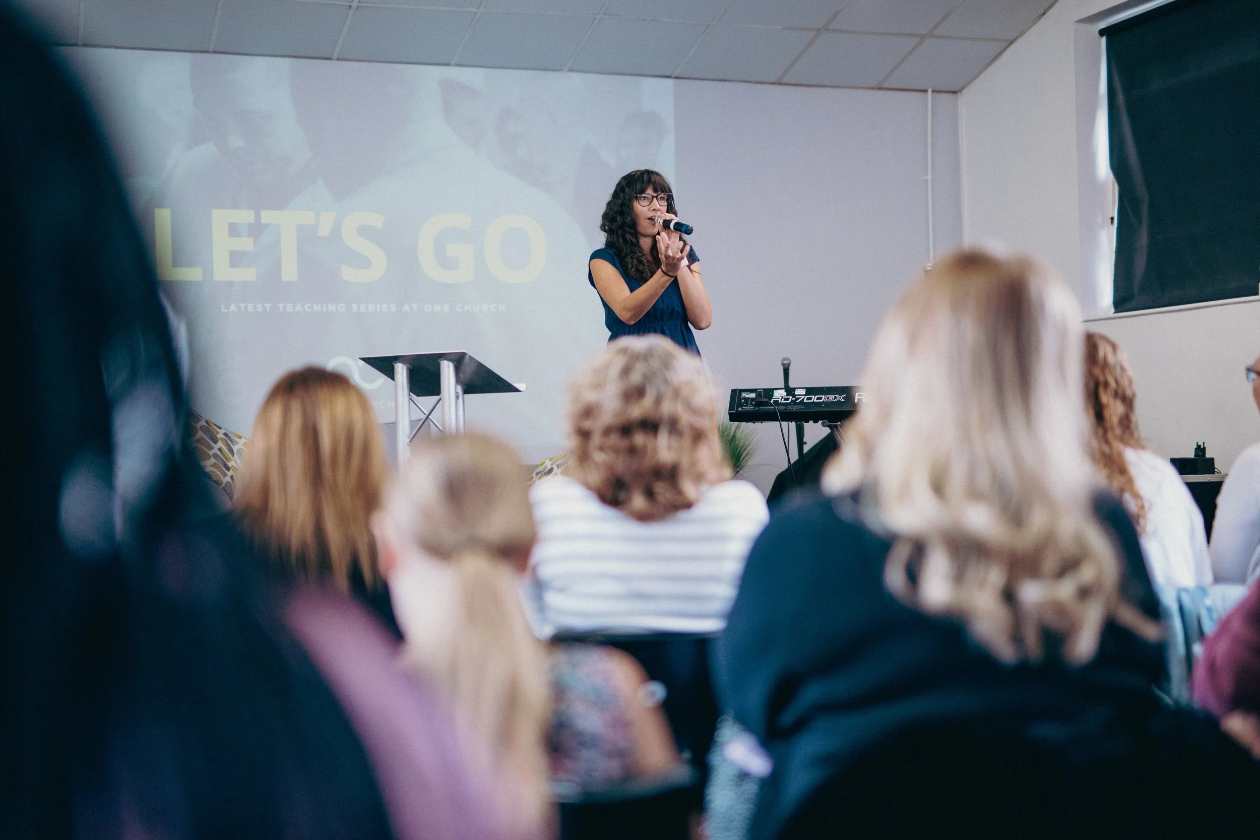 Indoor Christmas concert with people gathered, decorated with string lights, a Christmas tree, and a stage with musicians.