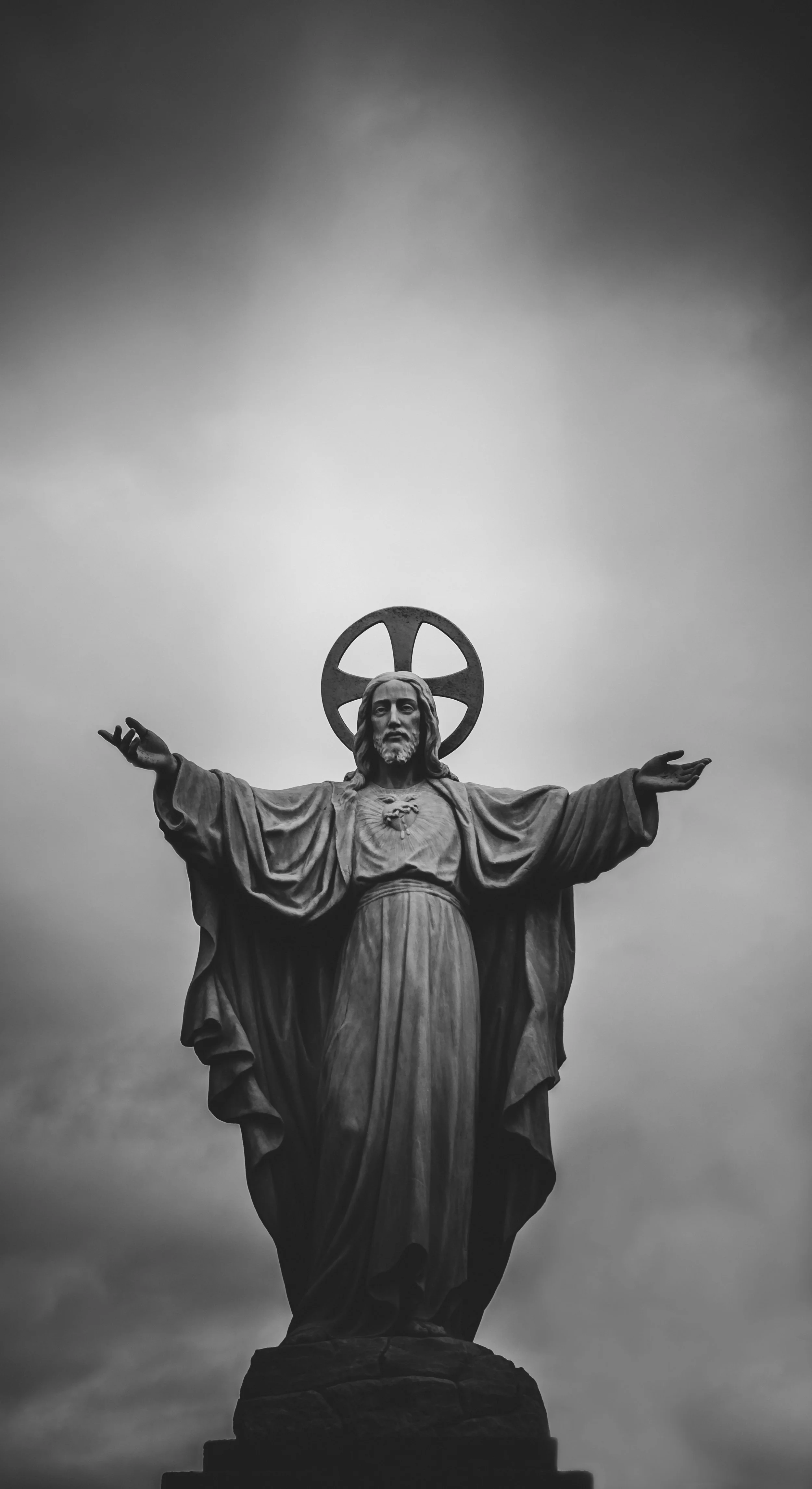 Black and white photograph of a large statue of Jesus Christ with open arms, standing on a pedestal against a cloudy sky.