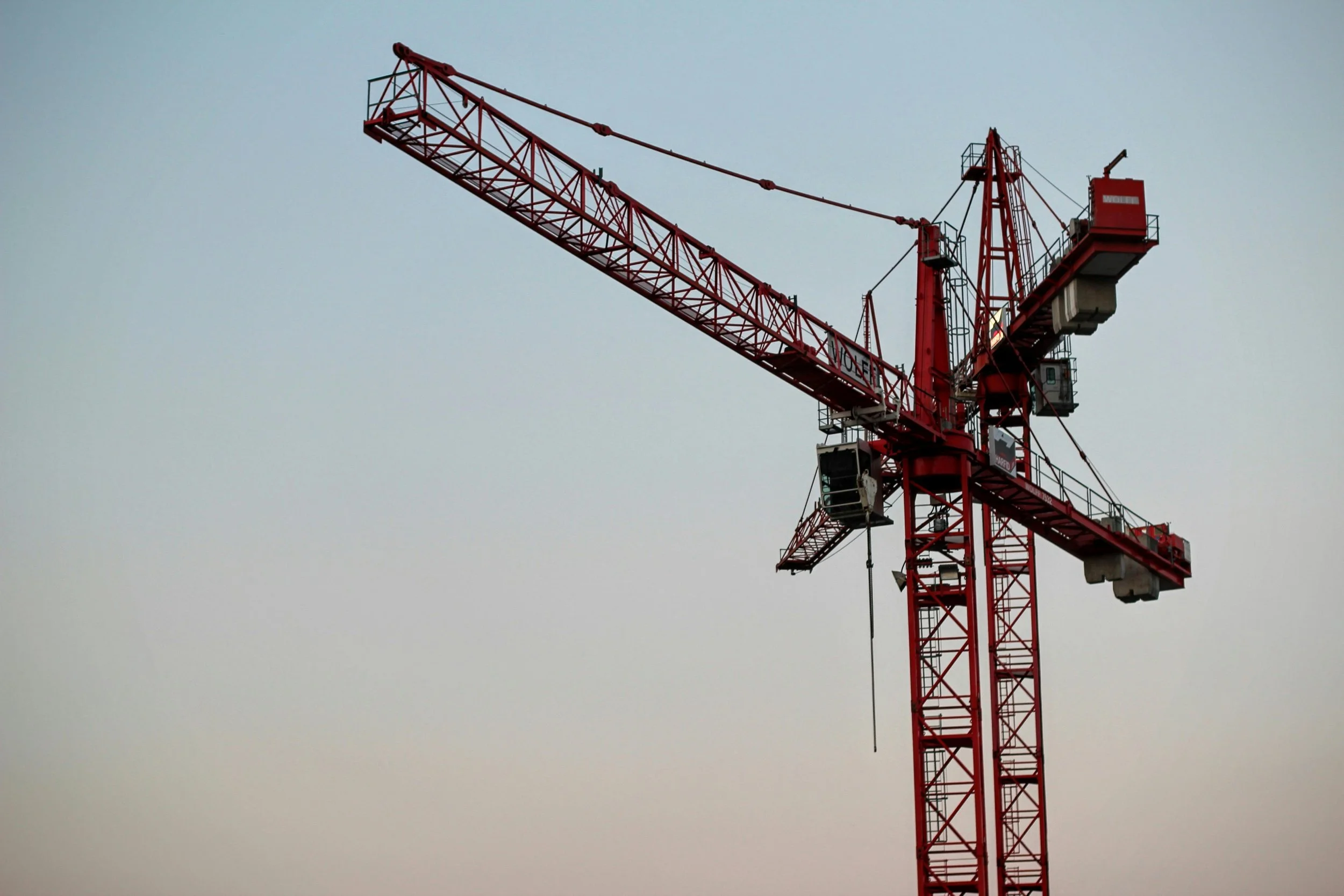 A large red construction tower crane against a light bluish sky.