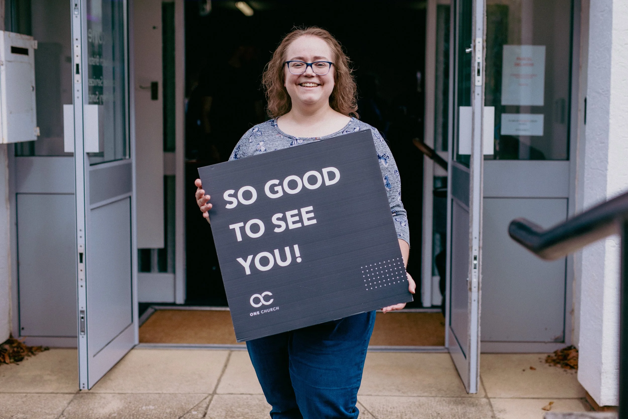 A group of diverse adults engaging in conversation in an indoor setting, with a blue curtain in the background.