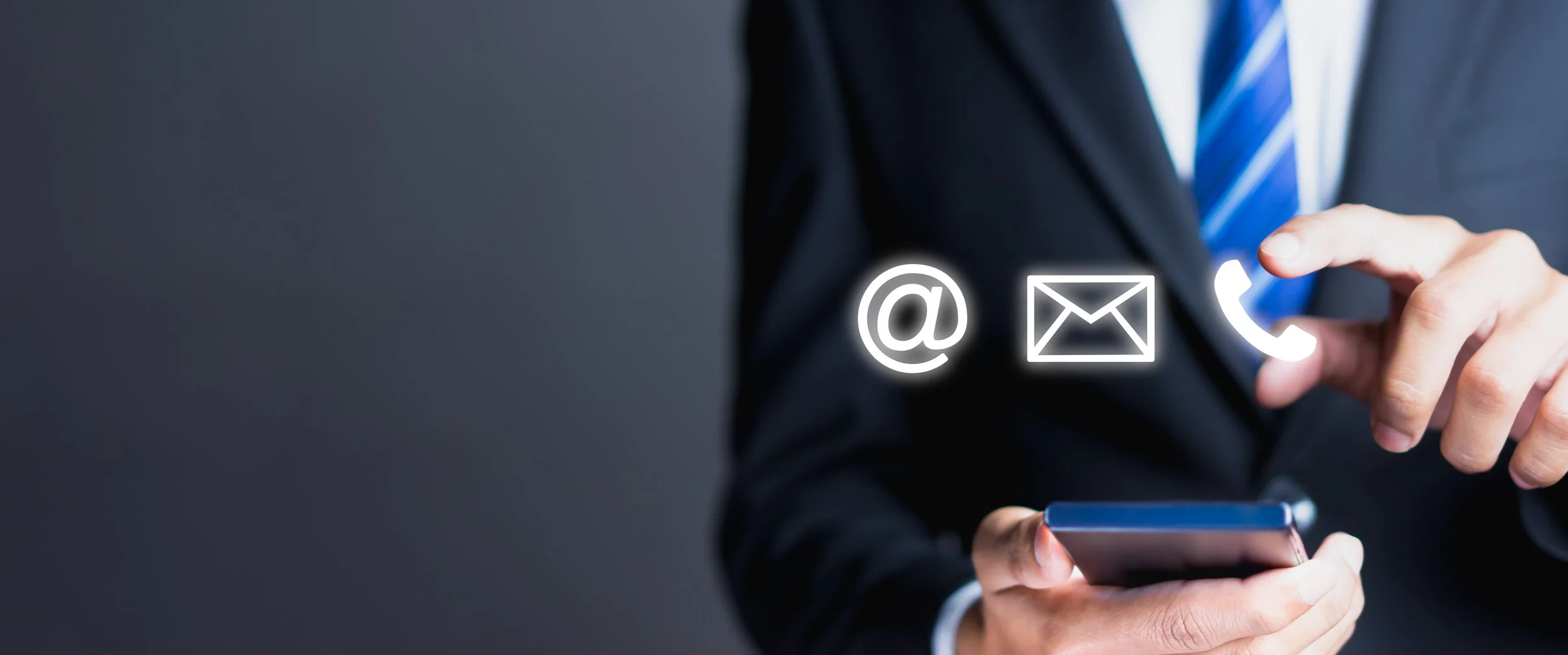 A person in a business suit using a smartphone with holographic icons of contact methods: at sign, email envelope, and phone receiver.
