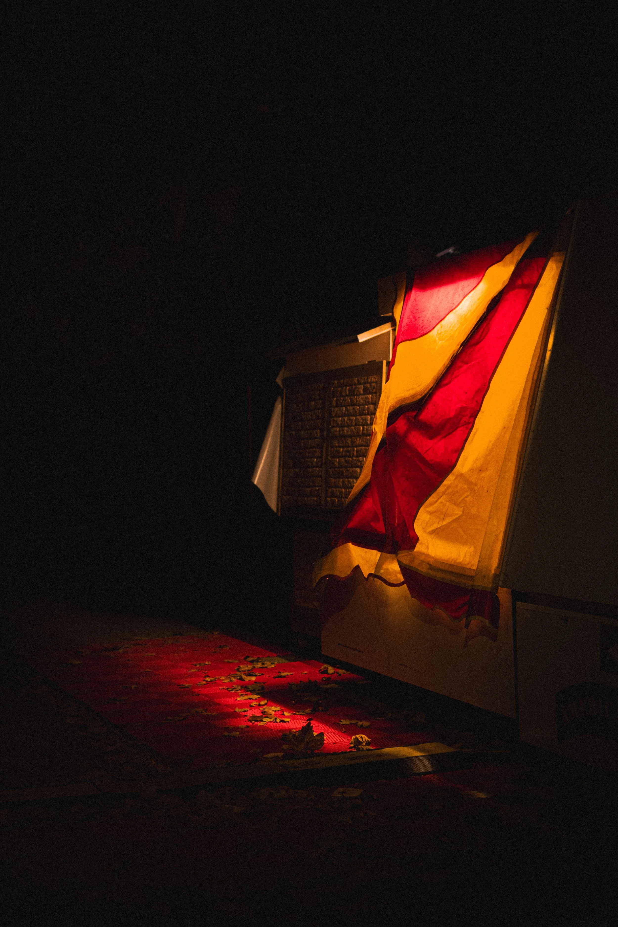 Tente en tissu coloré doucement éclairée dans l’obscurité, avec un tapis rouge et jaune à motifs posé au sol.