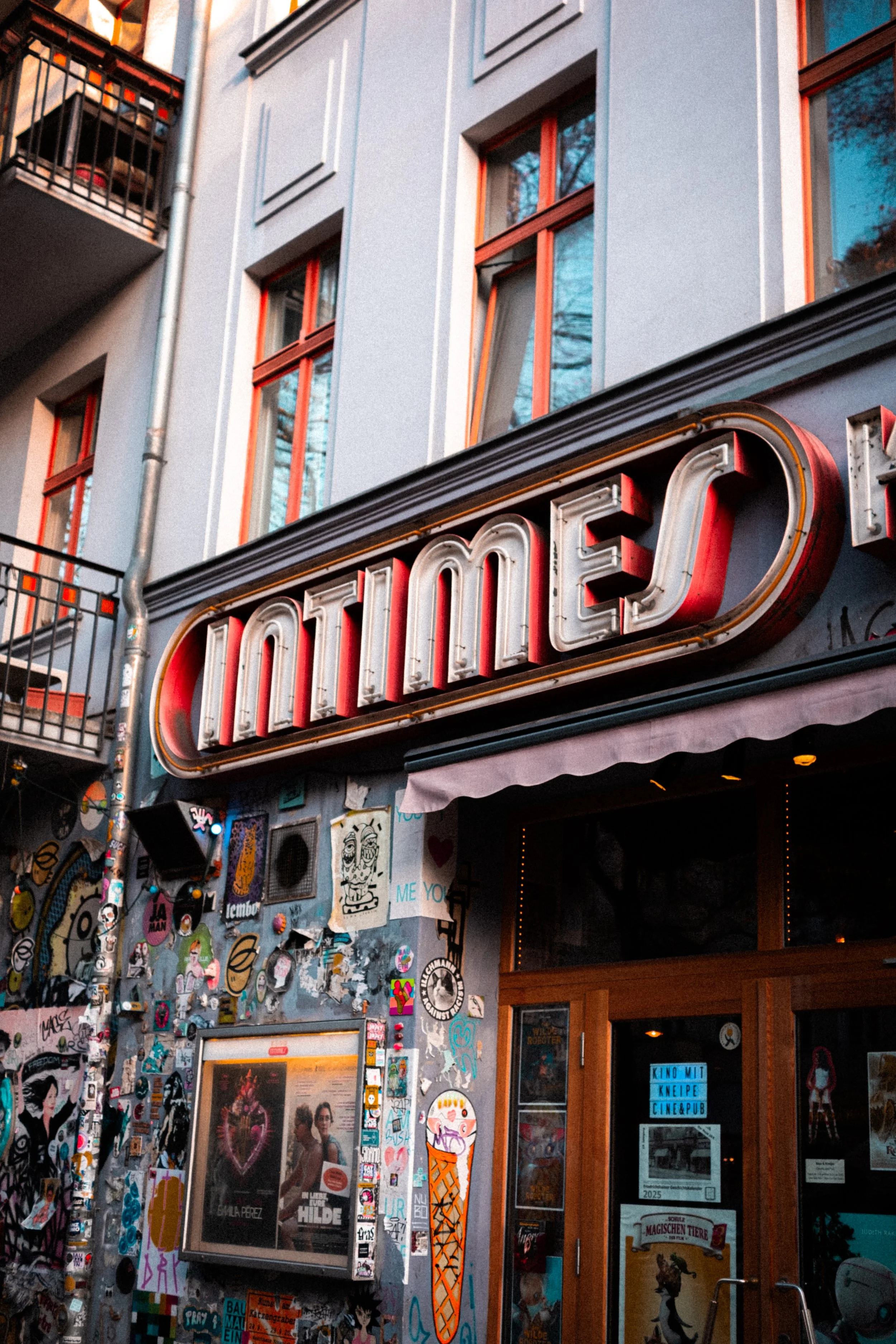 
Gros plan sur une façade de bâtiment avec enseigne vintage lumineuse "Movies", mur couvert d’autocollants, affiches et graffitis.