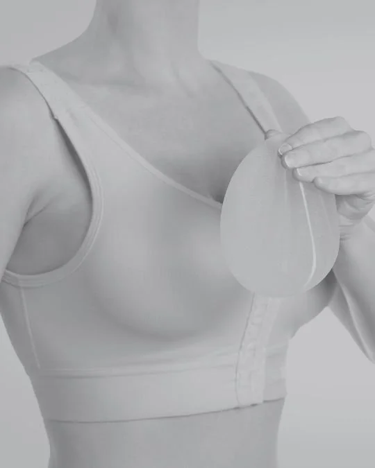 Woman in a post-surgical support bra holding a breast implant, illustrating planning or recovery stage of a combined breast uplift and augmentation procedure.