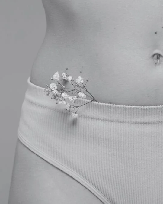 Minimalist image of a woman’s lower abdomen in underwear with delicate flowers tucked at the hip, symbolising femininity and the gentle nature of labiaplasty procedures.
