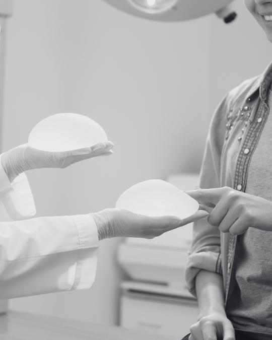 doctor holding two breast implants with a woman touching one