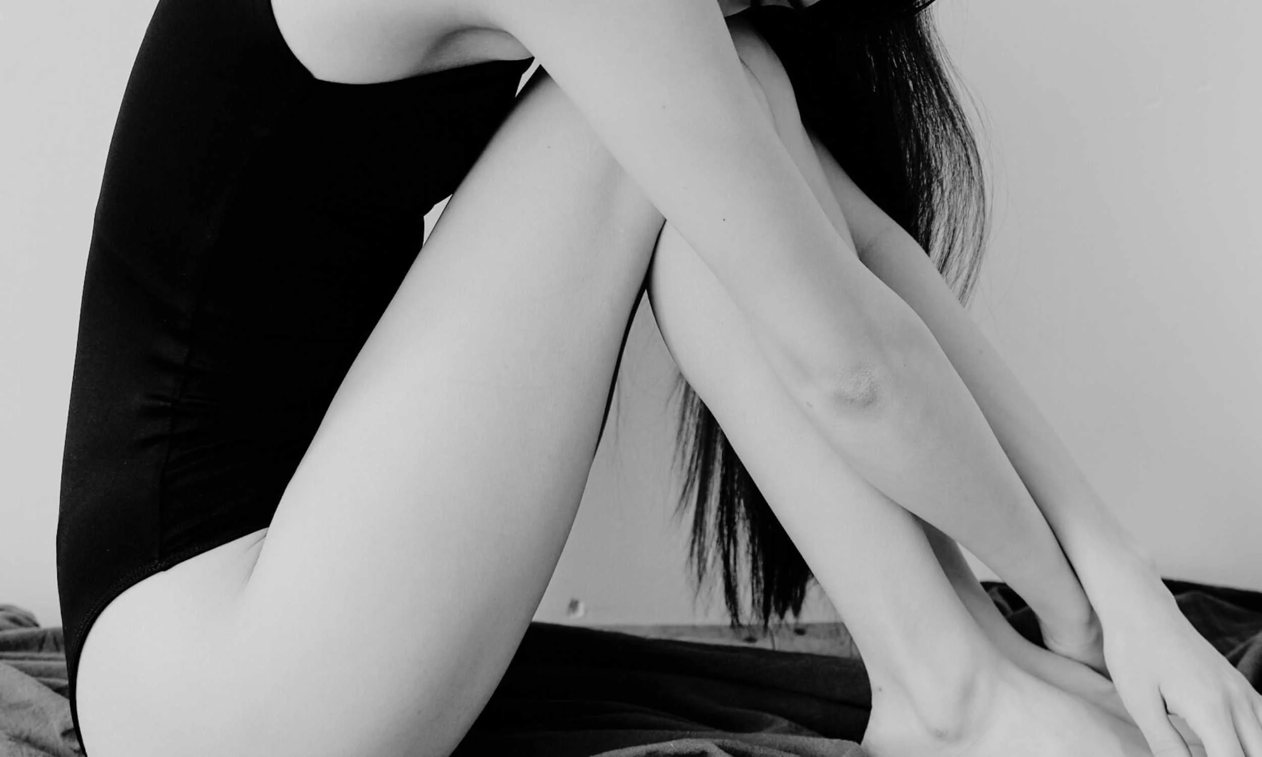 A black and white photo of a woman sitting with her knees up, arms wrapped around her legs.