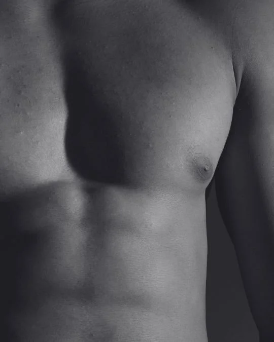 Subtle side-lit image of a male chest and upper abdomen showing natural contours and flatness following gynaecomastia correction.