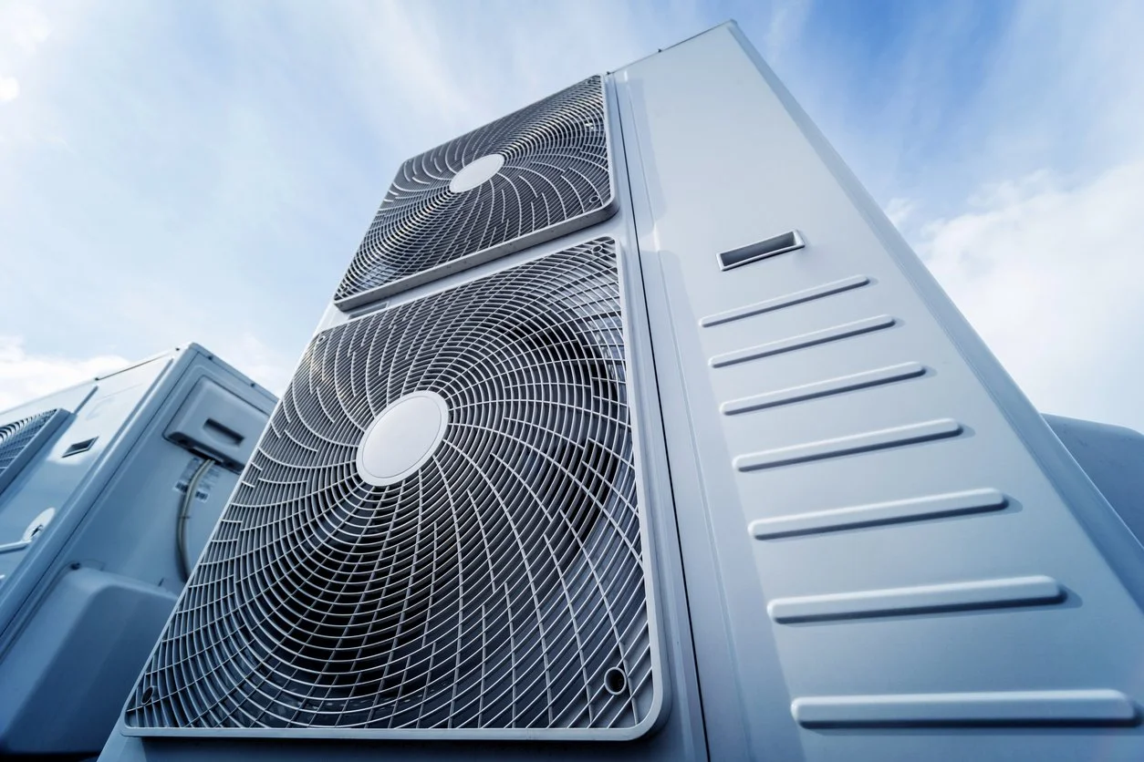 Large outdoor air conditioning units with two fans each, mounted on a building roof against a blue sky with scattered clouds.