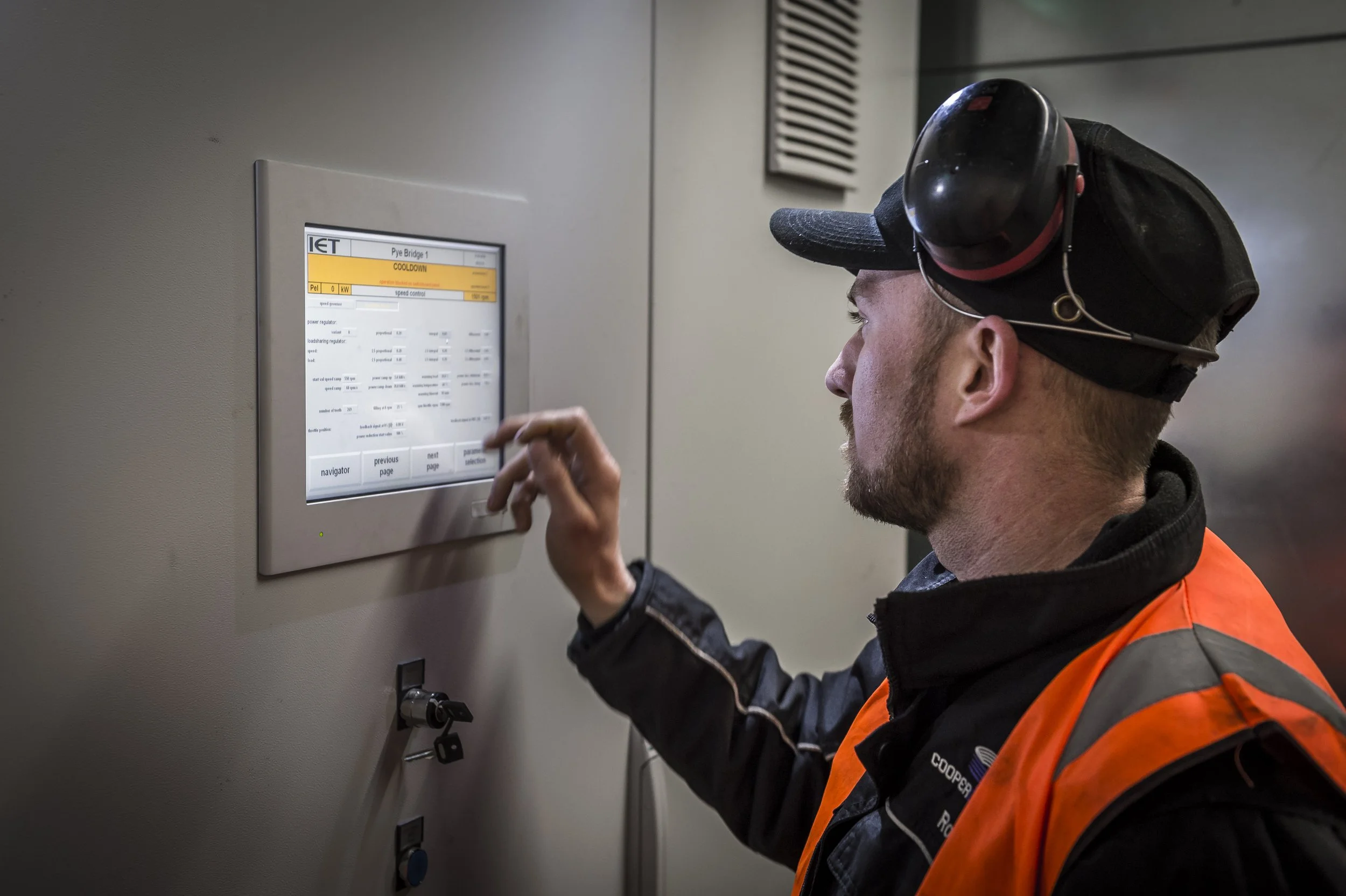 Man in safety vest and helmet operating control panel in industrial setting.