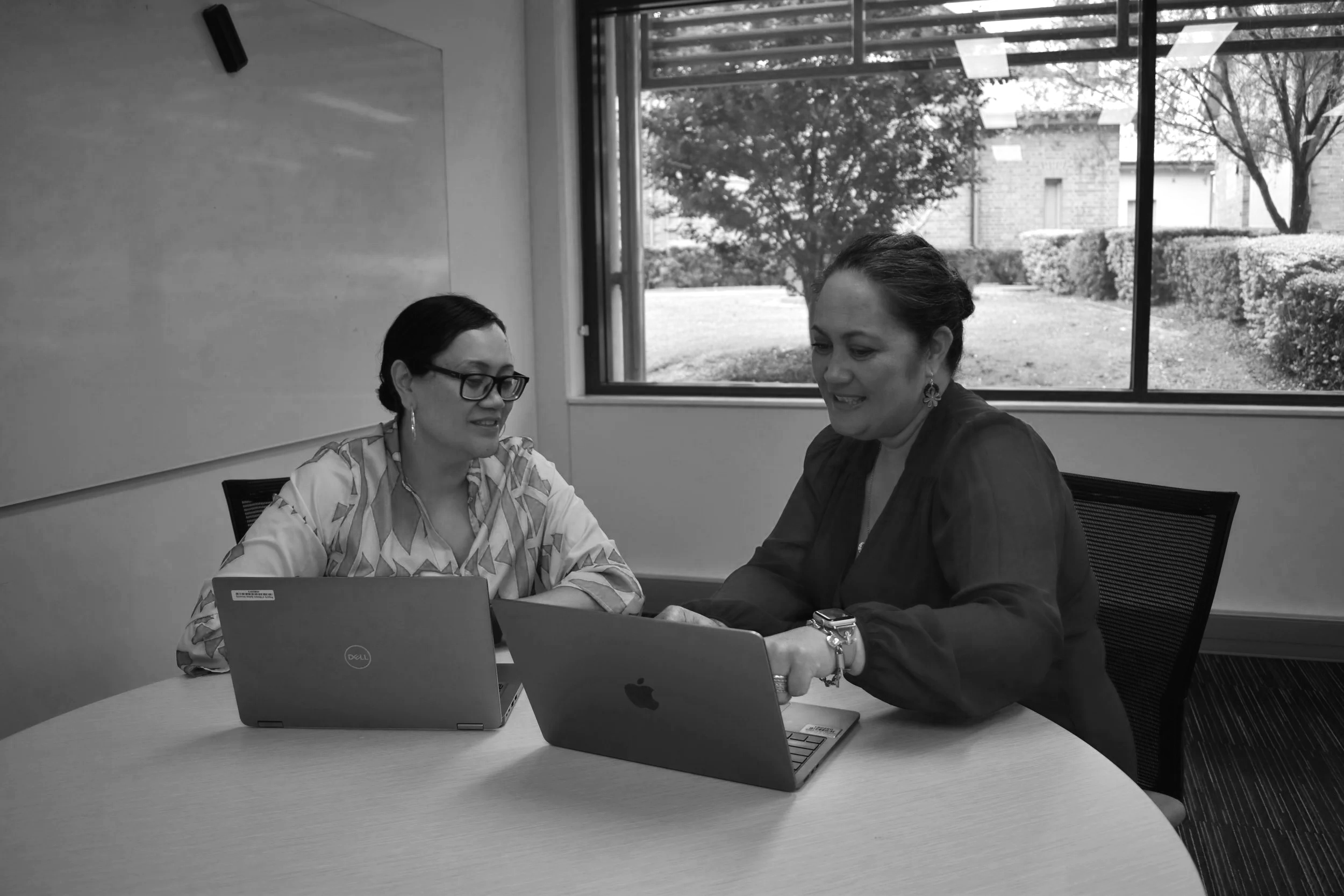 Amanda and Bronwyn sitting at a table looking at laptops in discussion