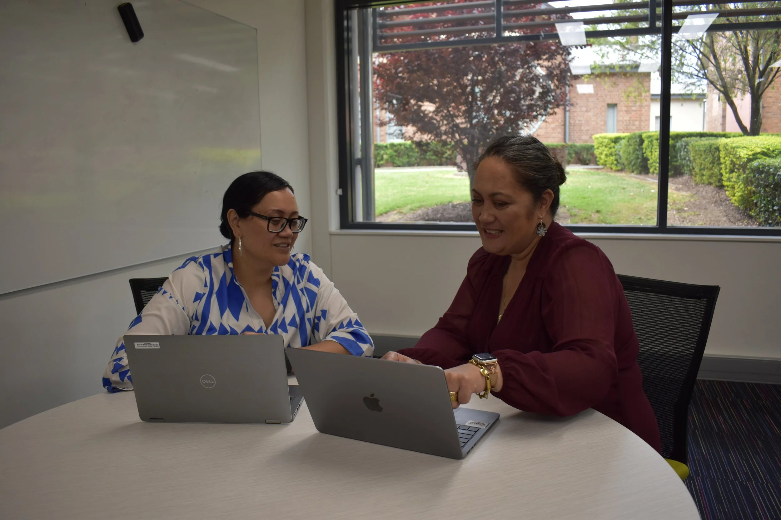 Amanda and Bronwyn sitting at a table looking at laptops in discussion
