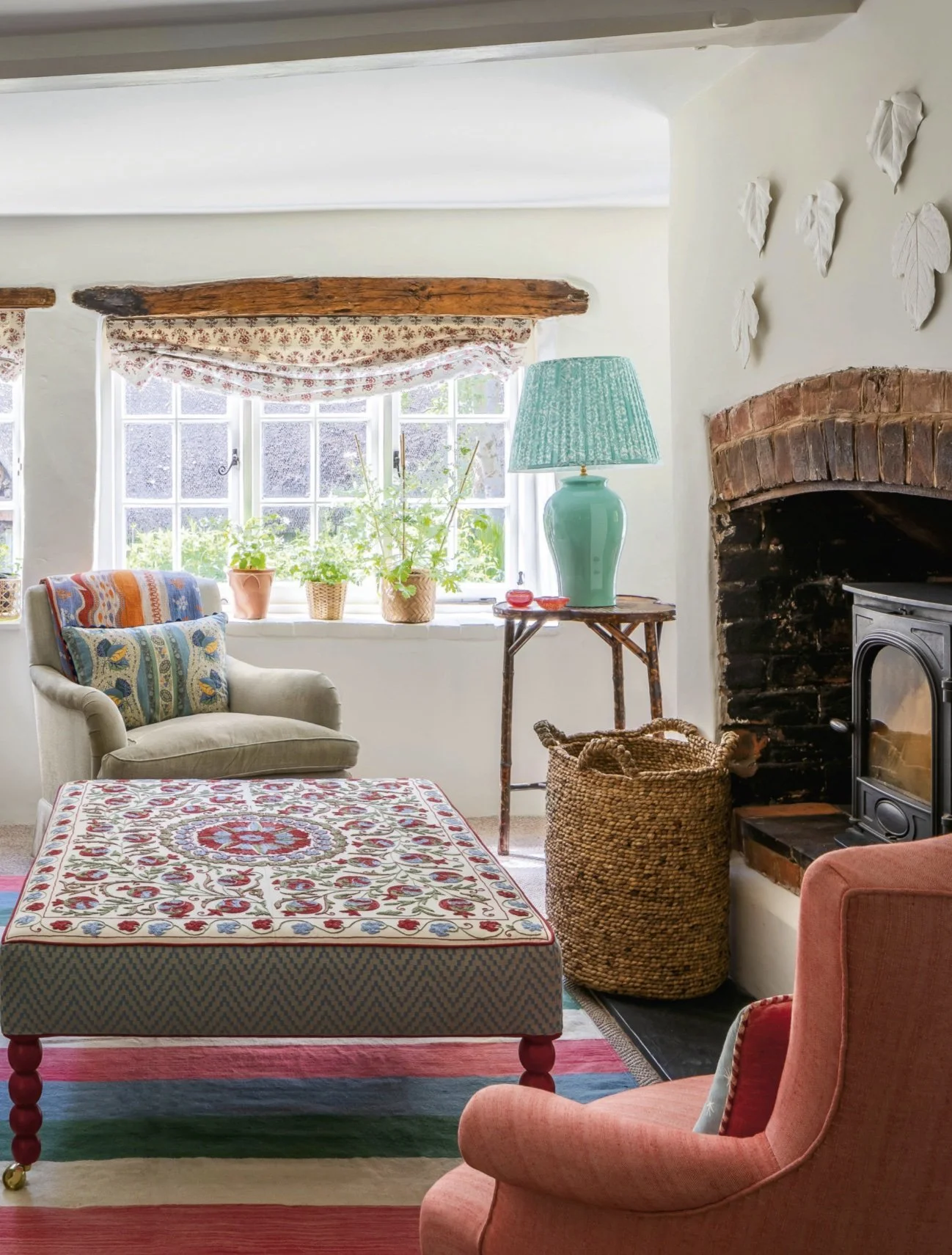 Cozy living room with a window, colorful patterned furniture, a lamp, potted plants, a stone fireplace, and a woven basket.