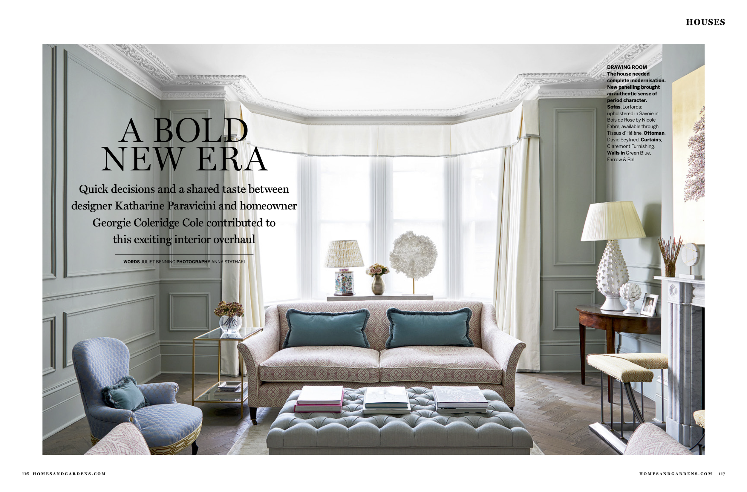 Elegant living room with pastel walls, large bay window, vintage sofa with teal pillows, blue armchair, tufted ottoman with books, side table with flowers, and floor lamp, decorated in a classic style.