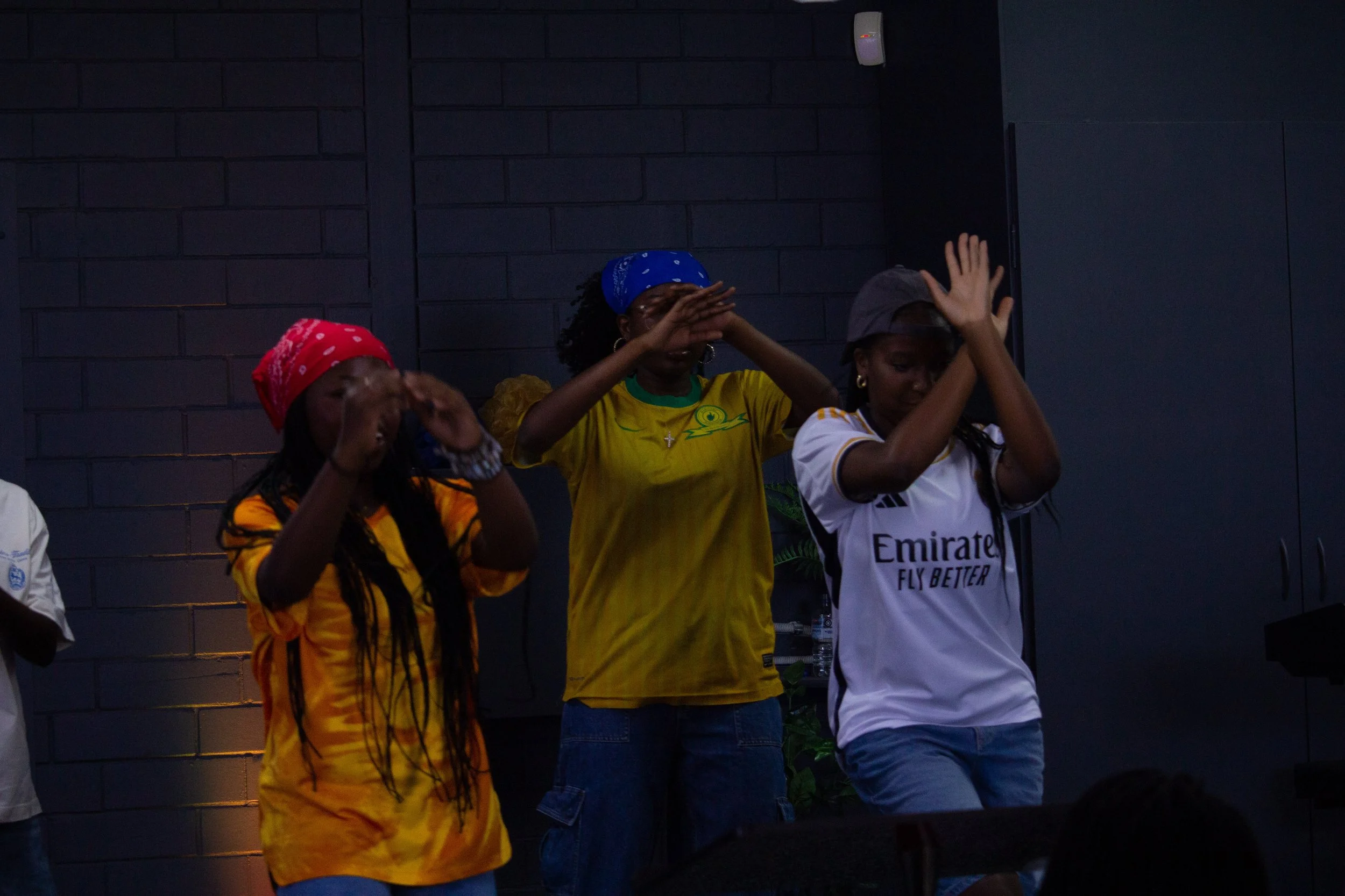 Greaterlife Church Youth members, raising their hands in front of their faces as if shielding their eyes from light or performing a dance move. Pictured at a Greaterlife Church Thanksgiving Service.