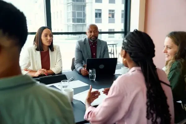 A diverse group of five academic professionals sitting around a conference table, engaged in a serious but collaborative discussion. This image illustrates the "human side" of a search committee working together to review candidates.