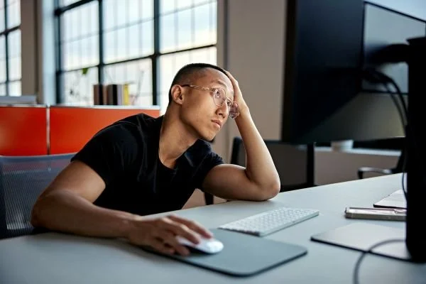 A young man at a computer looks distressed as he contemplates his professional life, symbolizing the need for setting professional boundaries. 