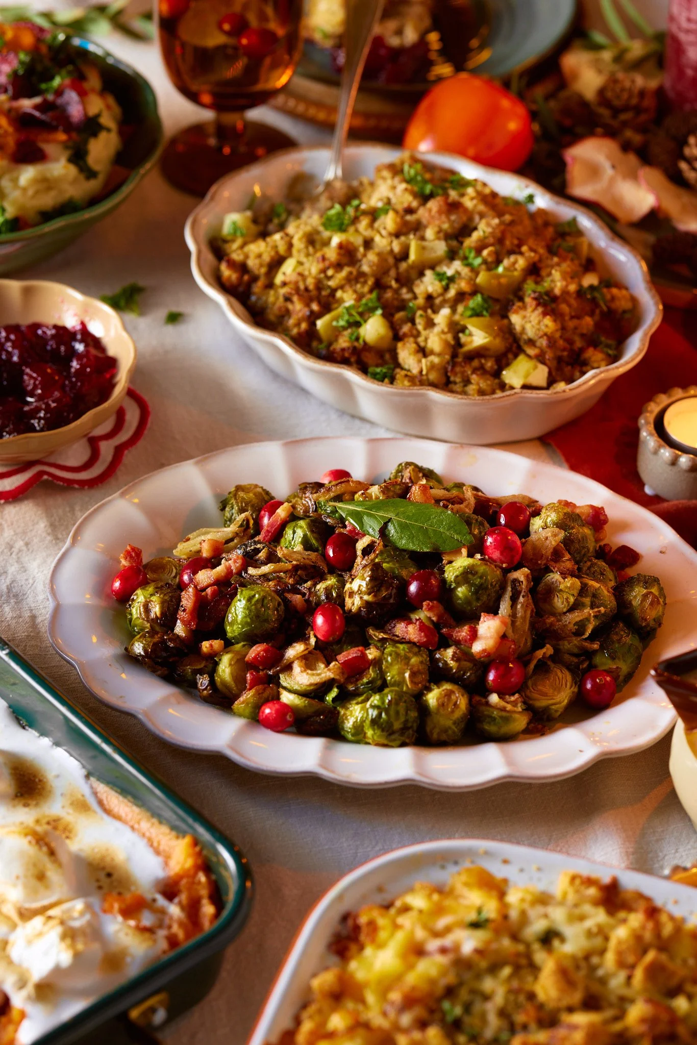 An assortment of Christmas dishes on a table, including Brussels sprouts with cranberries, stuffing with herbs, a salad, and mashed potatoes.