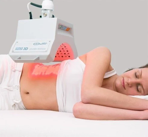 Vrouw ligt op haar zij tijdens een biofotonenbehandeling, de biofotonenlamp is gericht op haar buik.