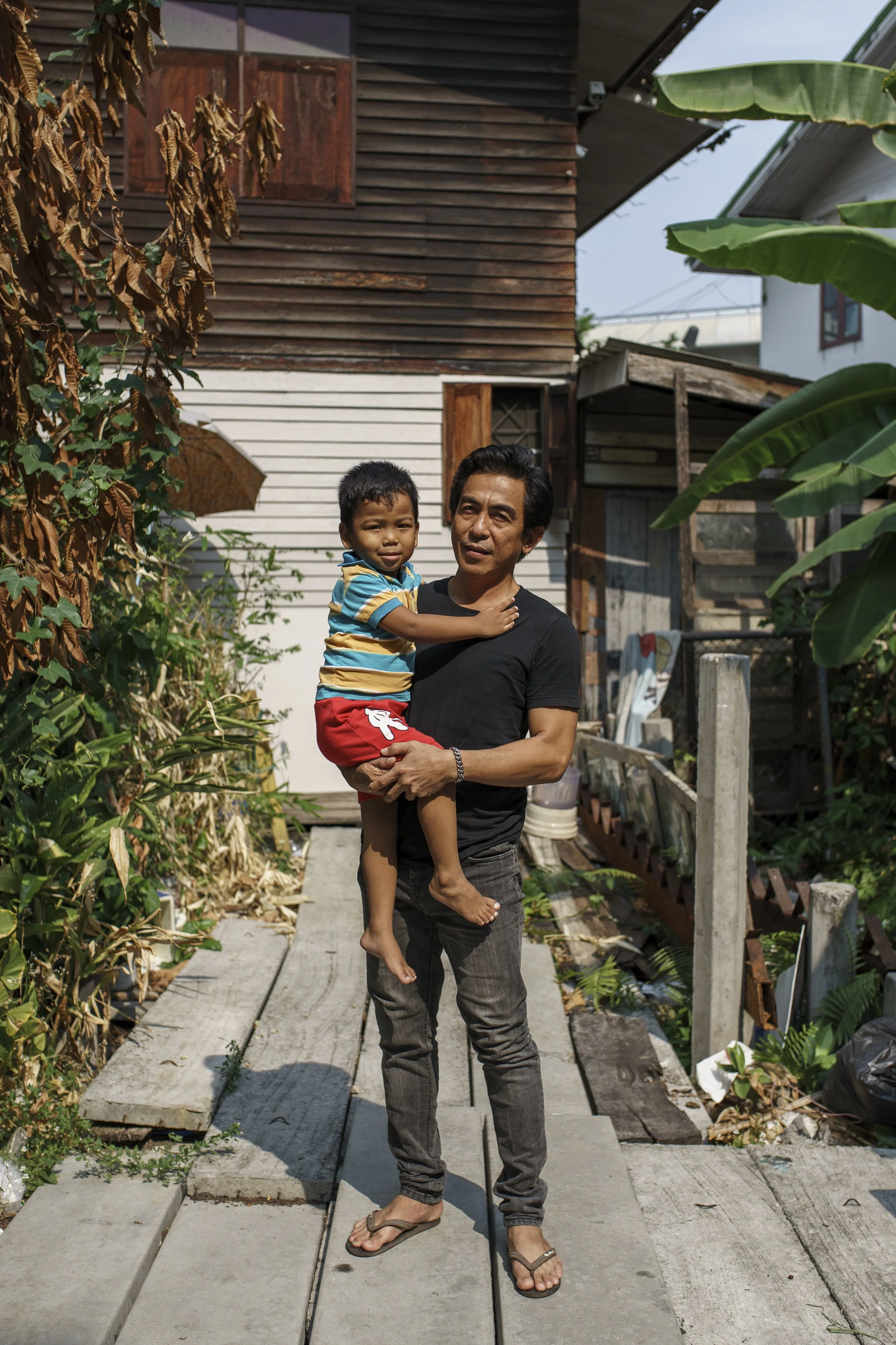 Sura Jitkusol, one of many residents in this community, holding his son in front of his house.
