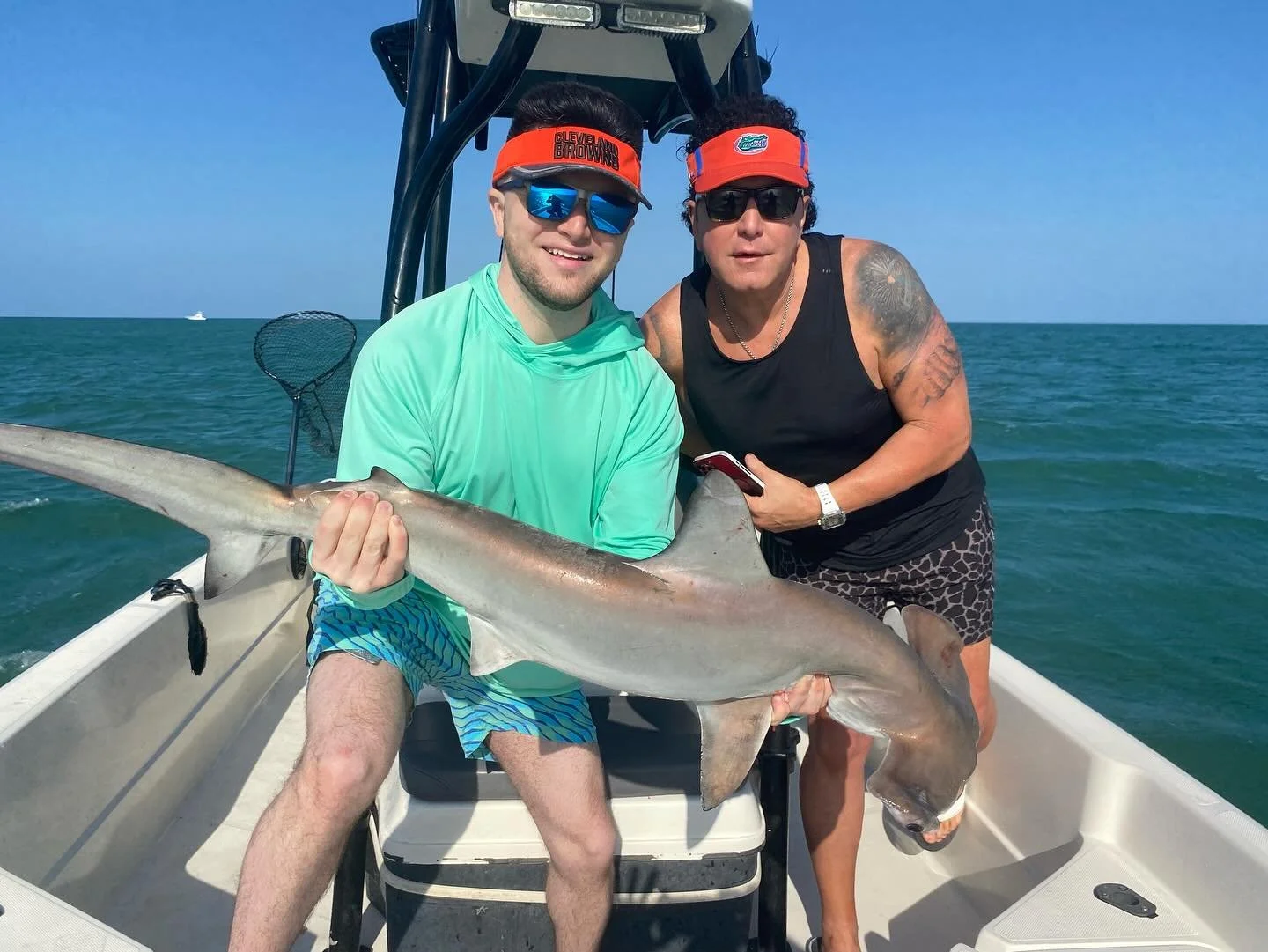 Two men on a boat holding a large fish, with ocean and blue sky in the background.