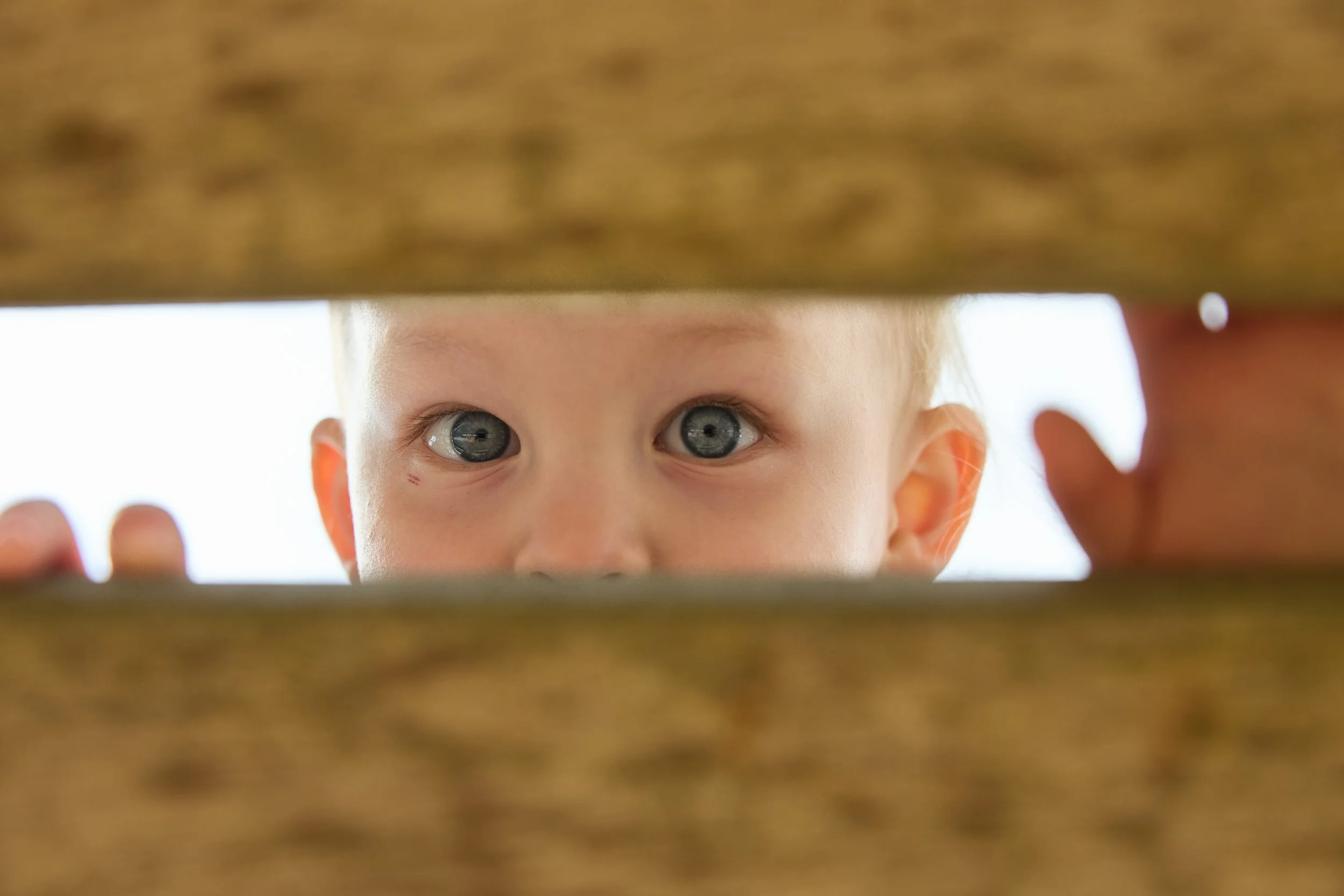 Nahaufnahme eines Jungen mit blauen Augen, der durch die Lücken eines Holzbodens schaut.