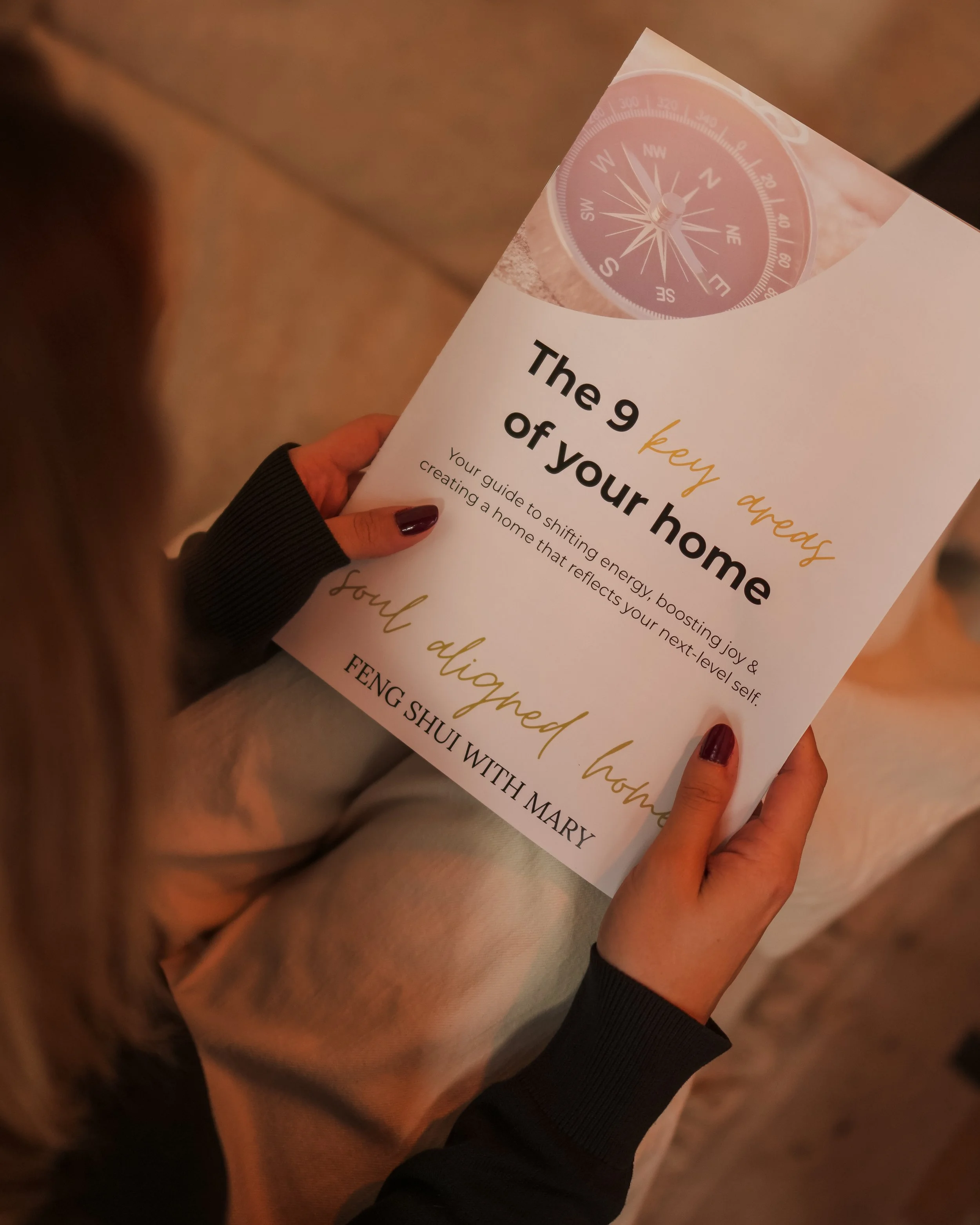 A person holding a brochure titled 'The 9 key ingredients of your home' with a compass graphic at the top and the text 'FENG SHUI WITH MARY' at the bottom.