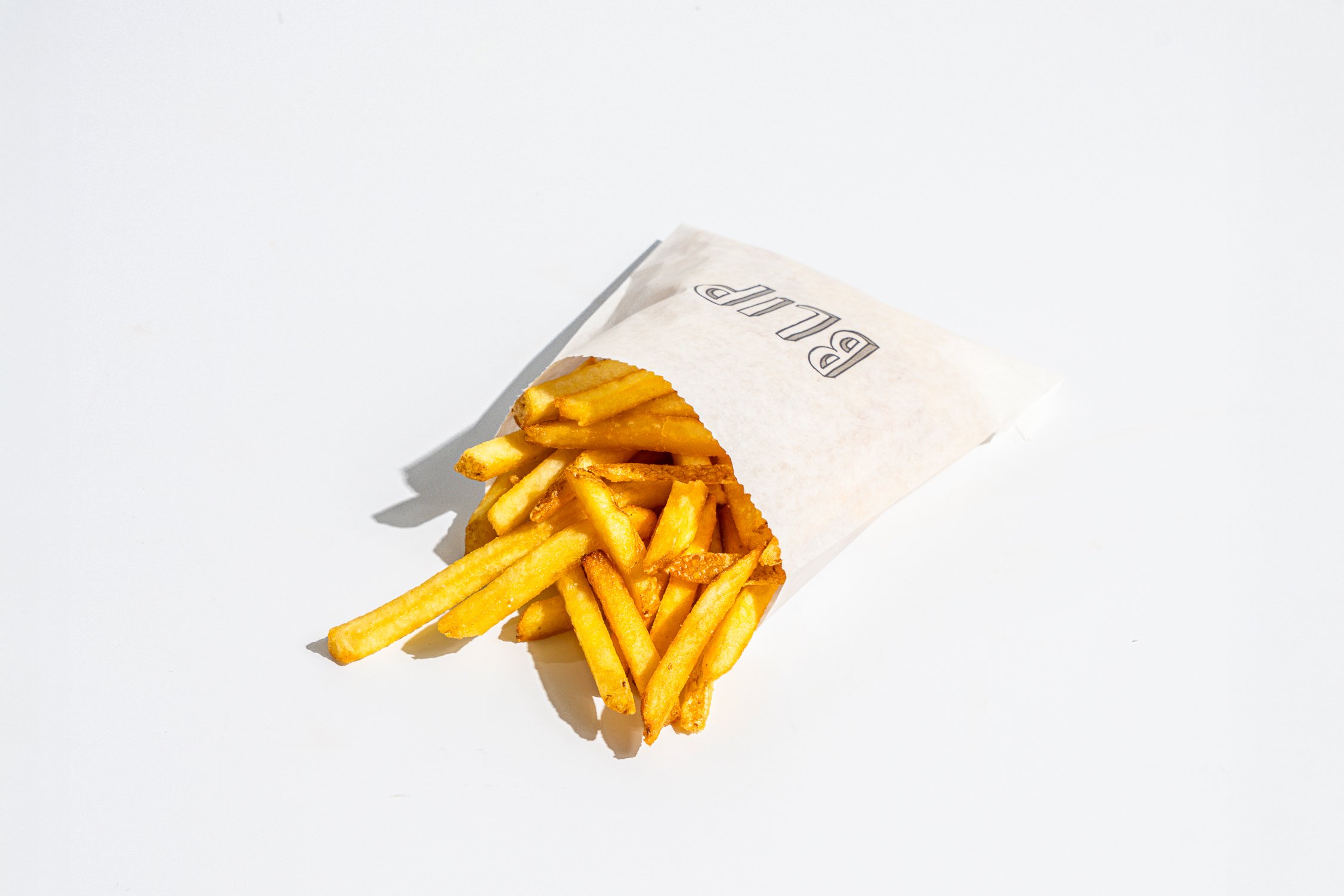 French fries spilling out of a paper bag on a white background.