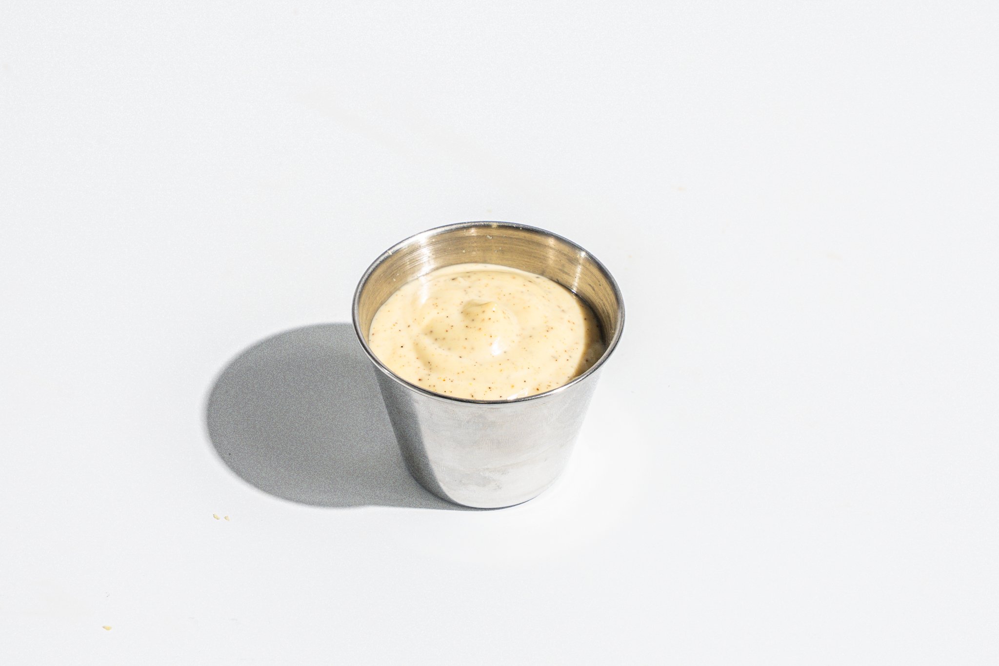 Metal tumbler filled with a creamy, speckled beverage on a white surface with a shadow.
