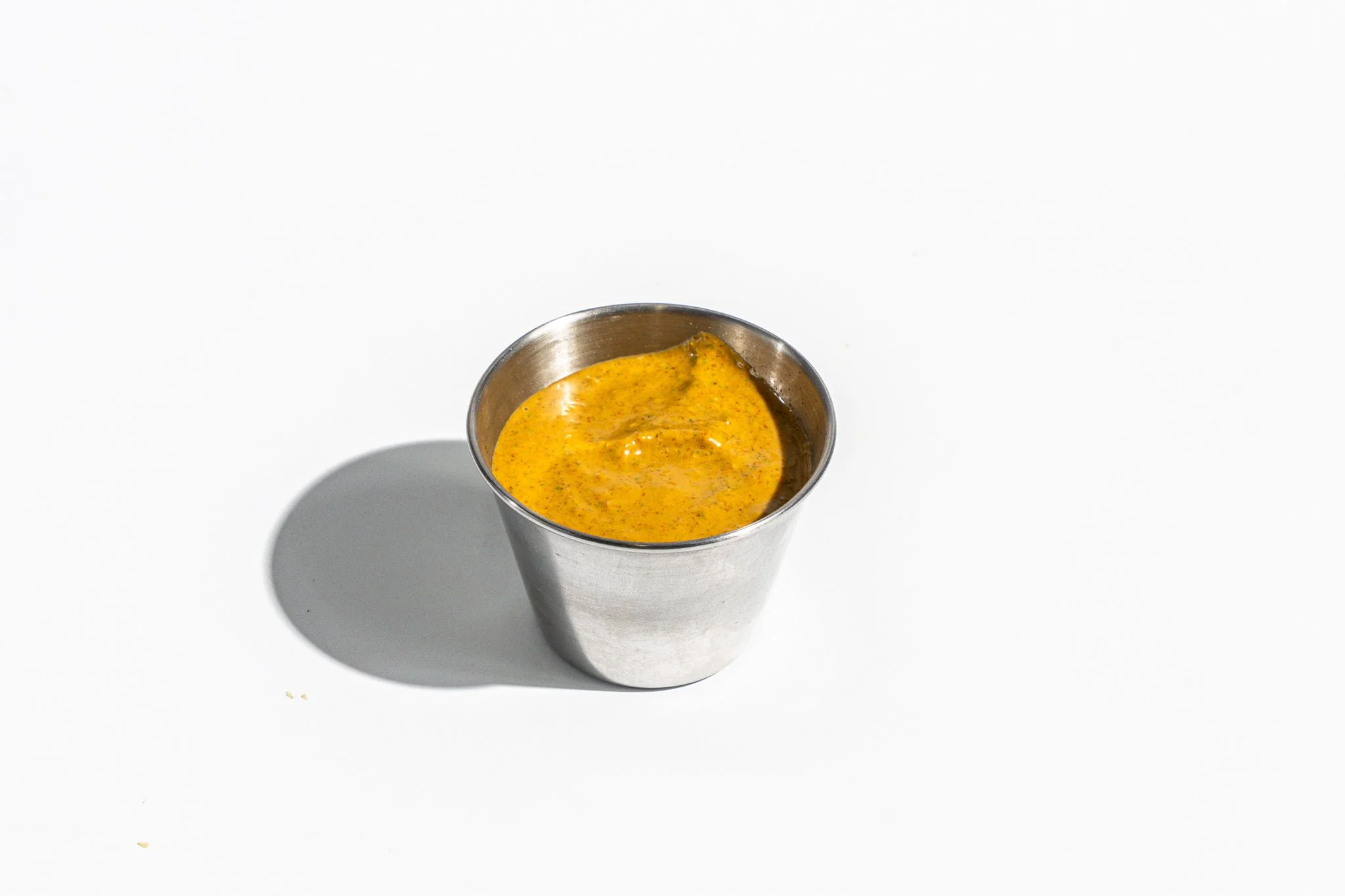 Cup of yellow curry sauce on a white background, with a shadow to the left.