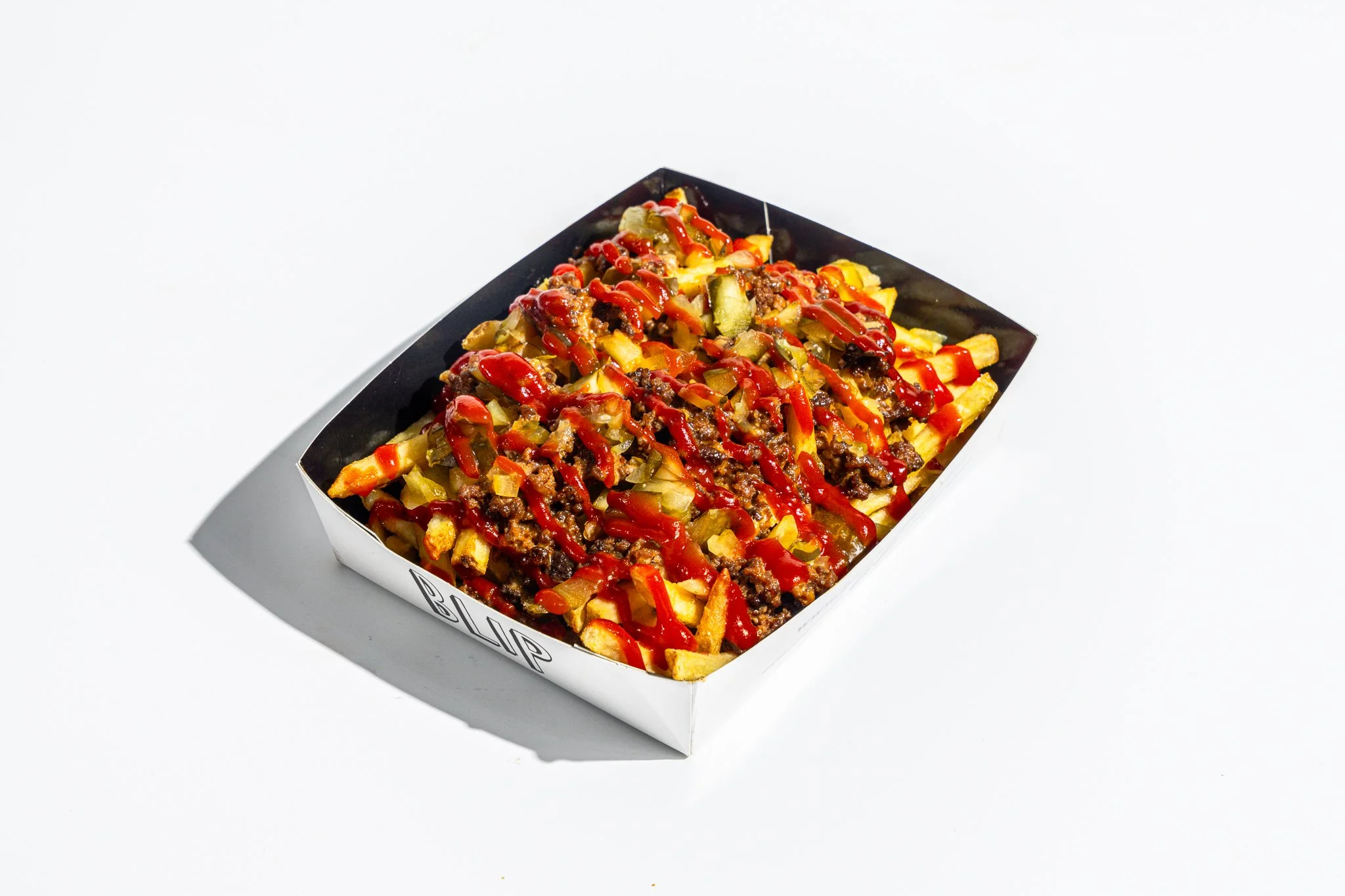 A serving tray filled with seasoned French fries topped with cooked ground beef, diced pickles, and ketchup.