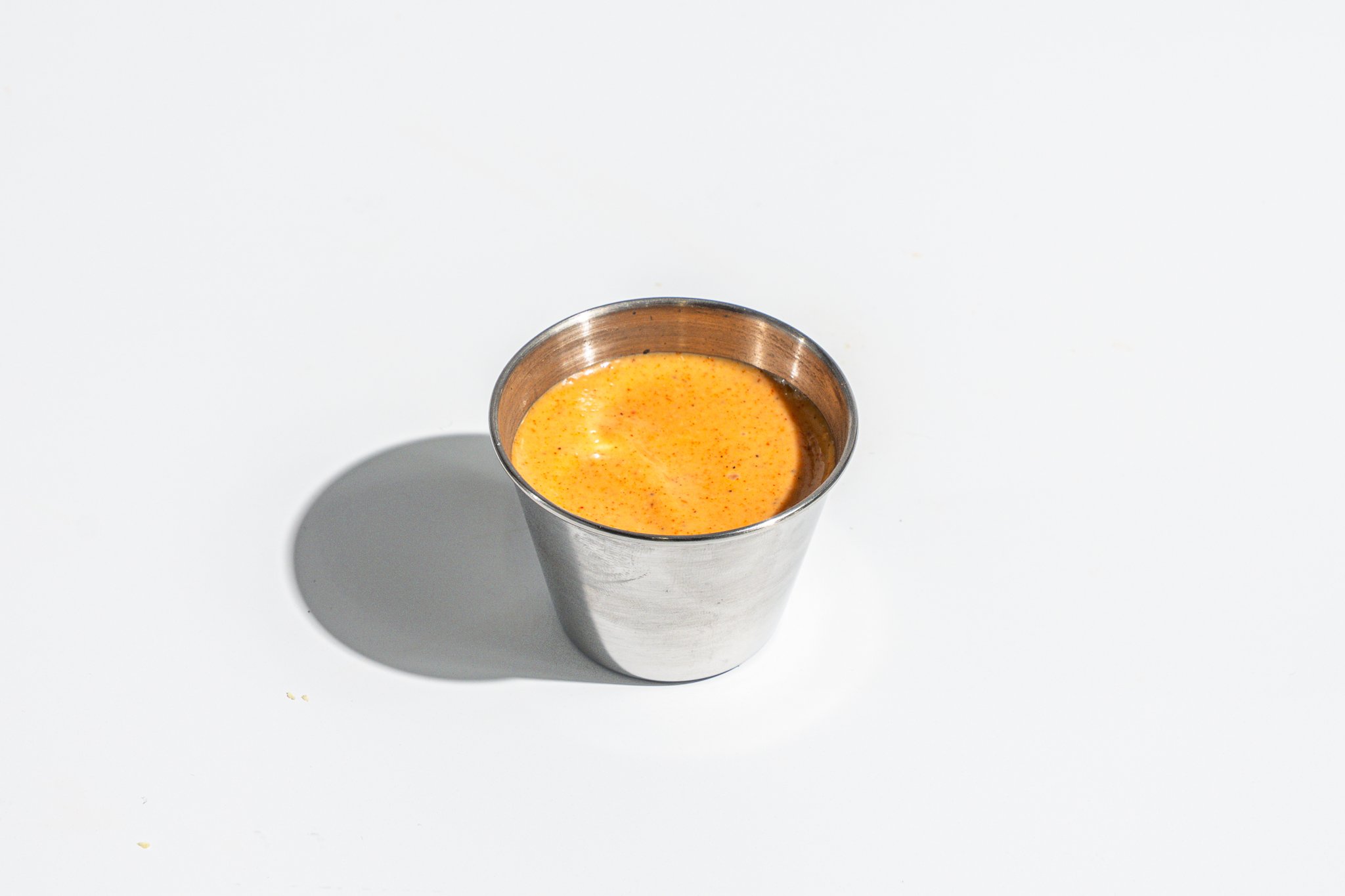 A metal cup filled with a yellow-orange drink on a white surface, casting a shadow to the left.